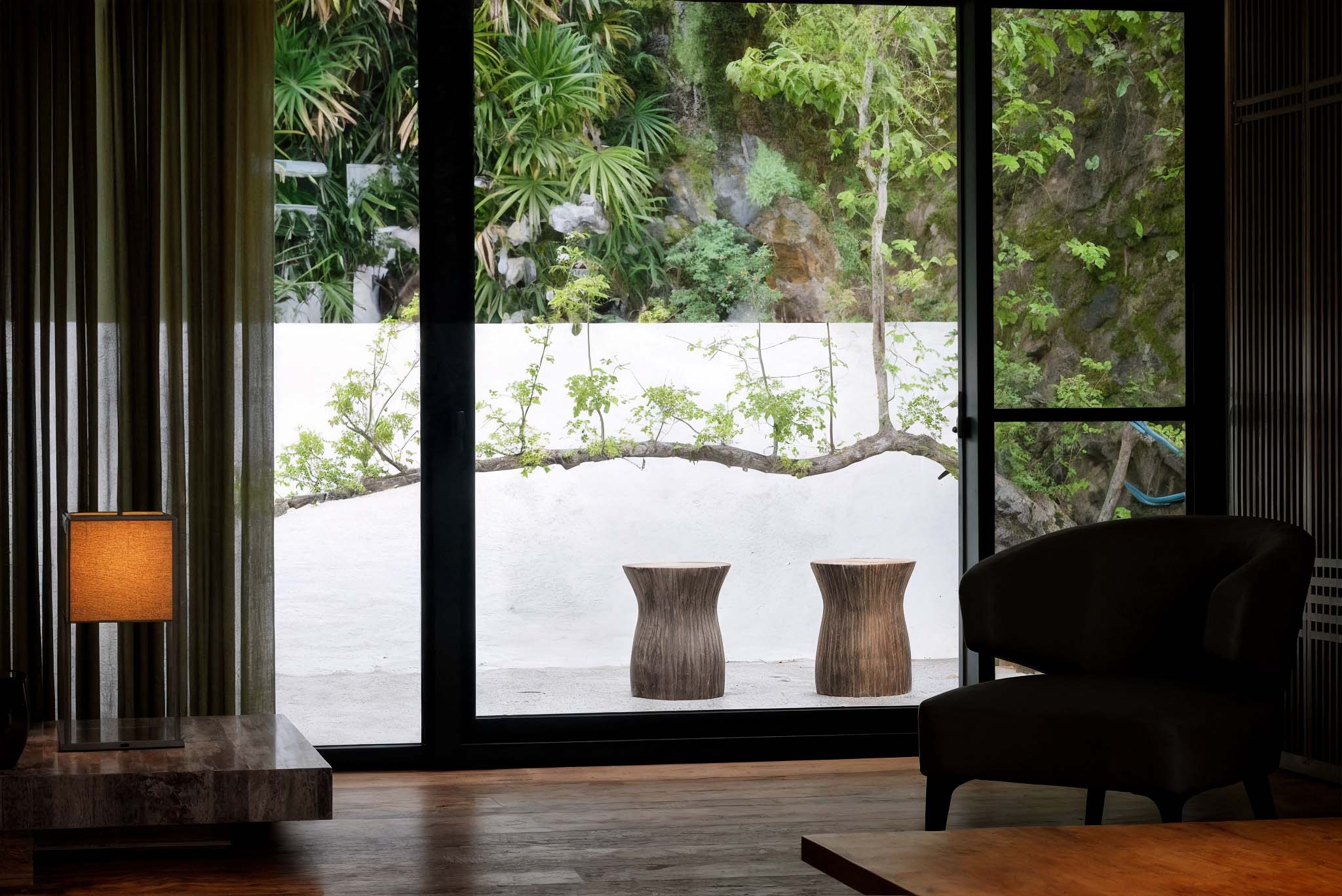 室內空間透過大片玻璃門望向戶外，白牆與蜿蜒樹枝搭配兩張木凳，形成寧靜自然的過渡景觀