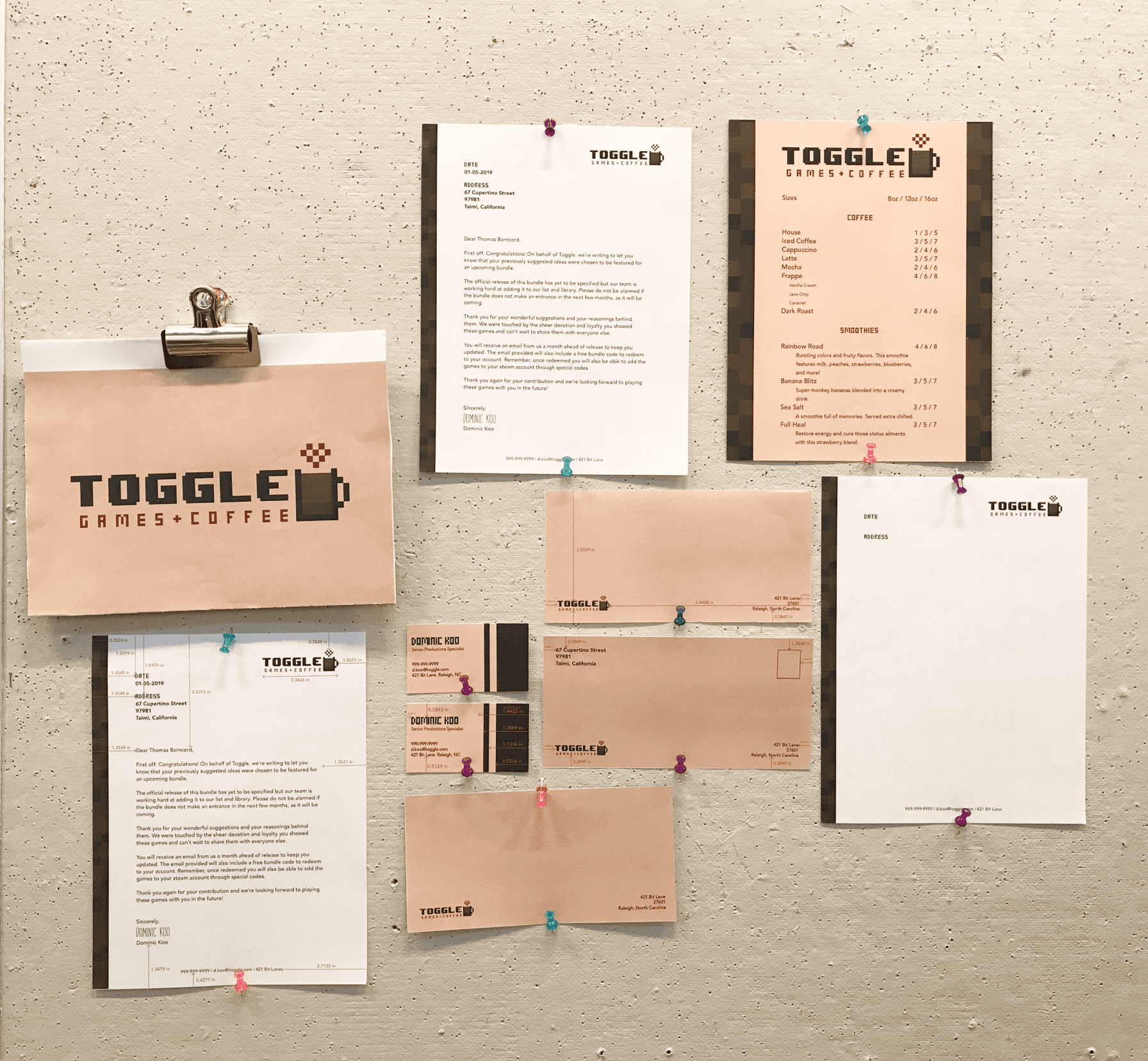 A wall-mounted collection of printed Toggle branding elements including menus, letters, and logos, clipped for critique.
