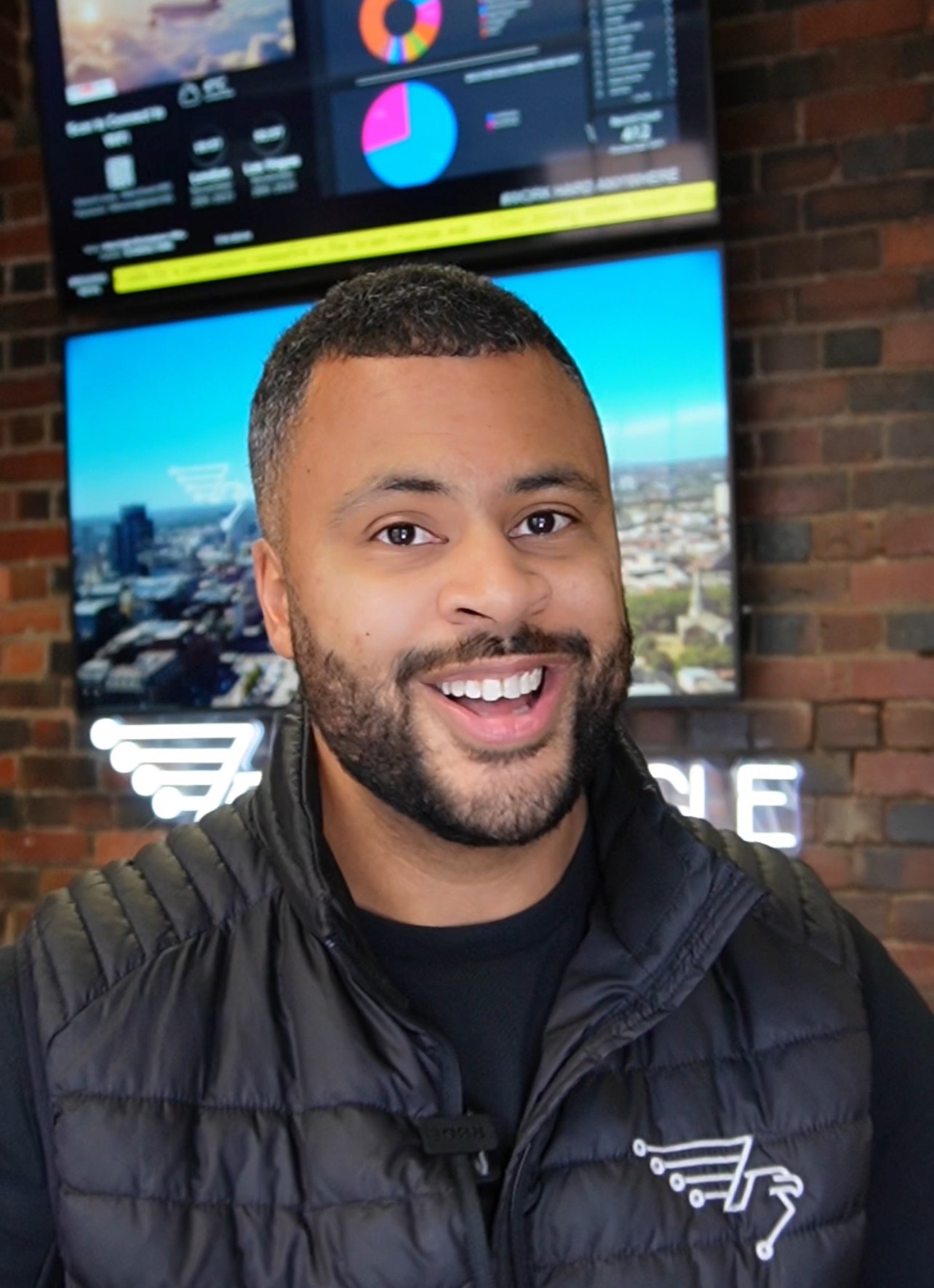 A woman with short curly hair wearing a black t-shirt looks into the camera.