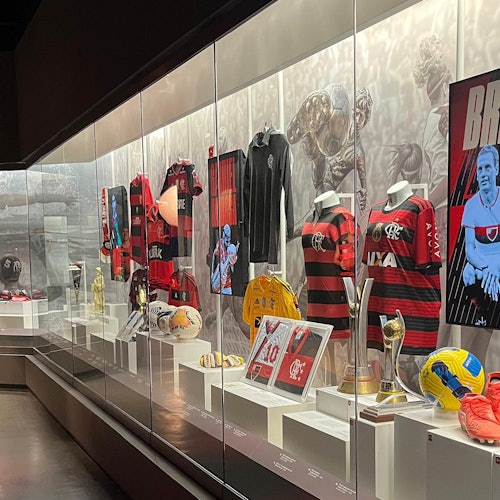 博物馆陈列柜展示红色和黑色的运动球衣、足球、奖杯和纪念品，包括照片和一张海报。