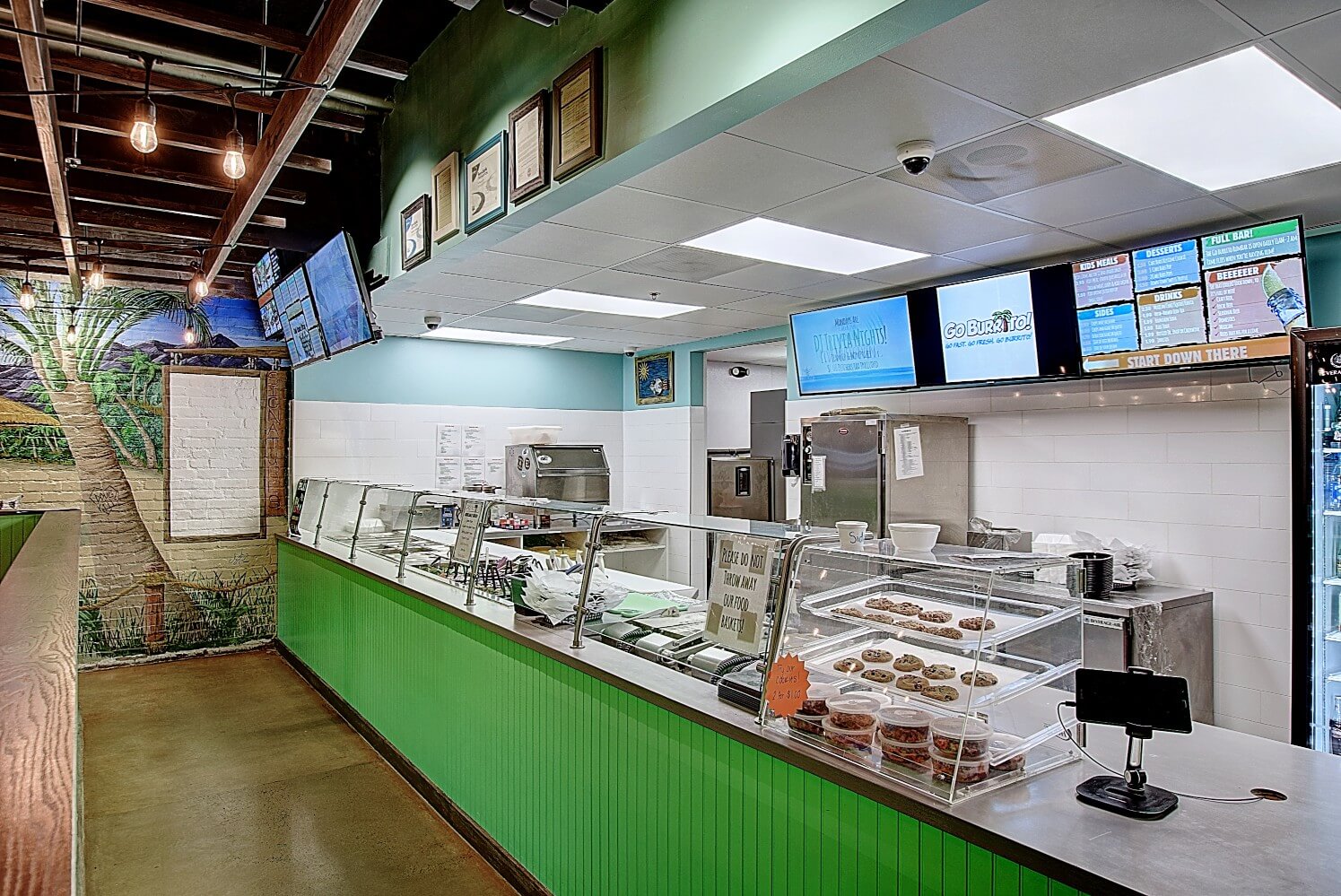 Modern fast-food restaurant interior with order counter, menu screens, and a colorful green accent wall.