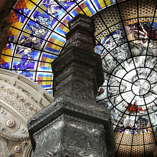 华丽的天花板搭配色彩斑斓的彩色玻璃窗和精美的雕刻，围绕着一个中央柱，上面有精致的浮雕。
