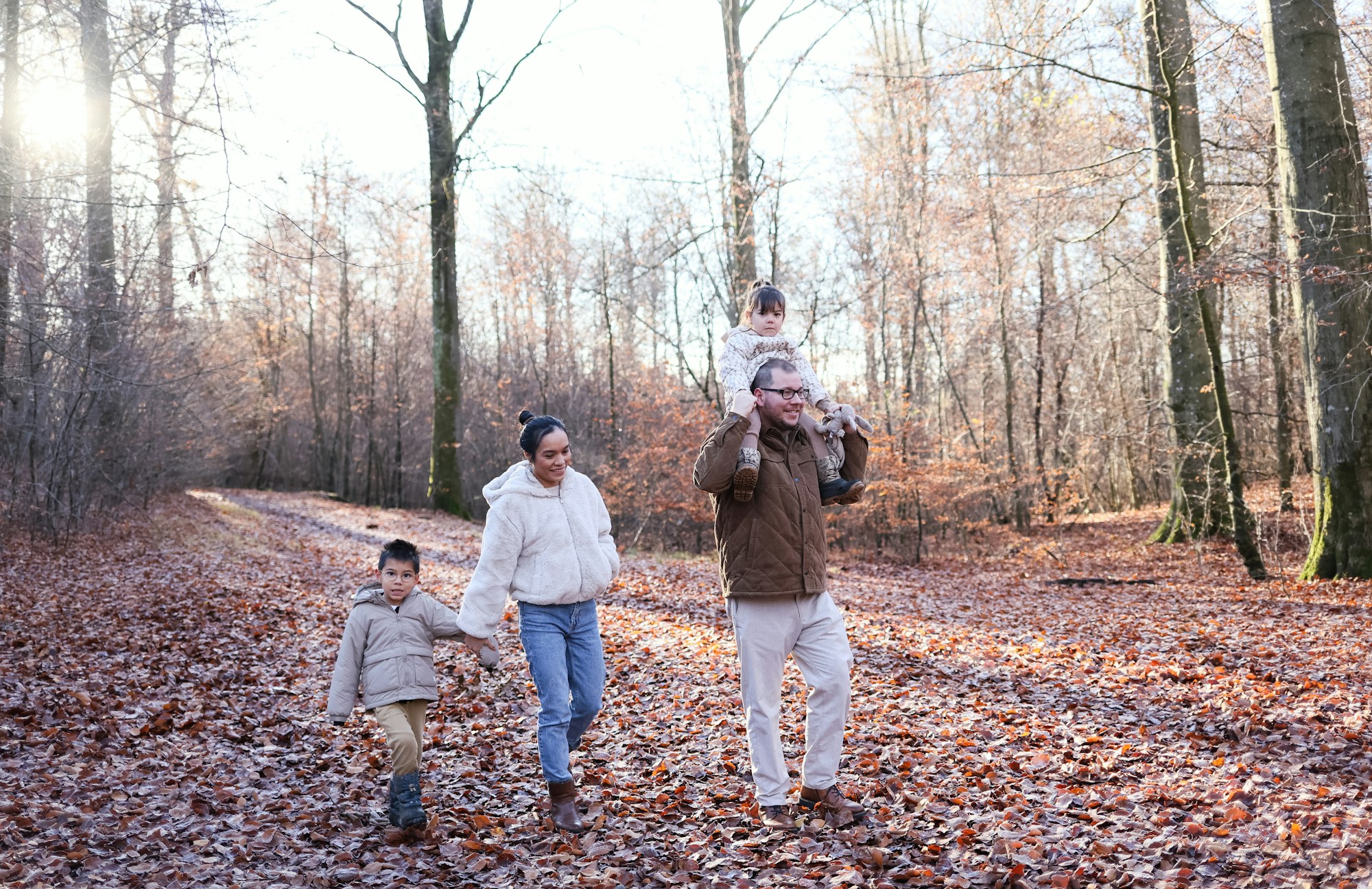 A family walking down a leafy woodland track, a child on dad's shoulders