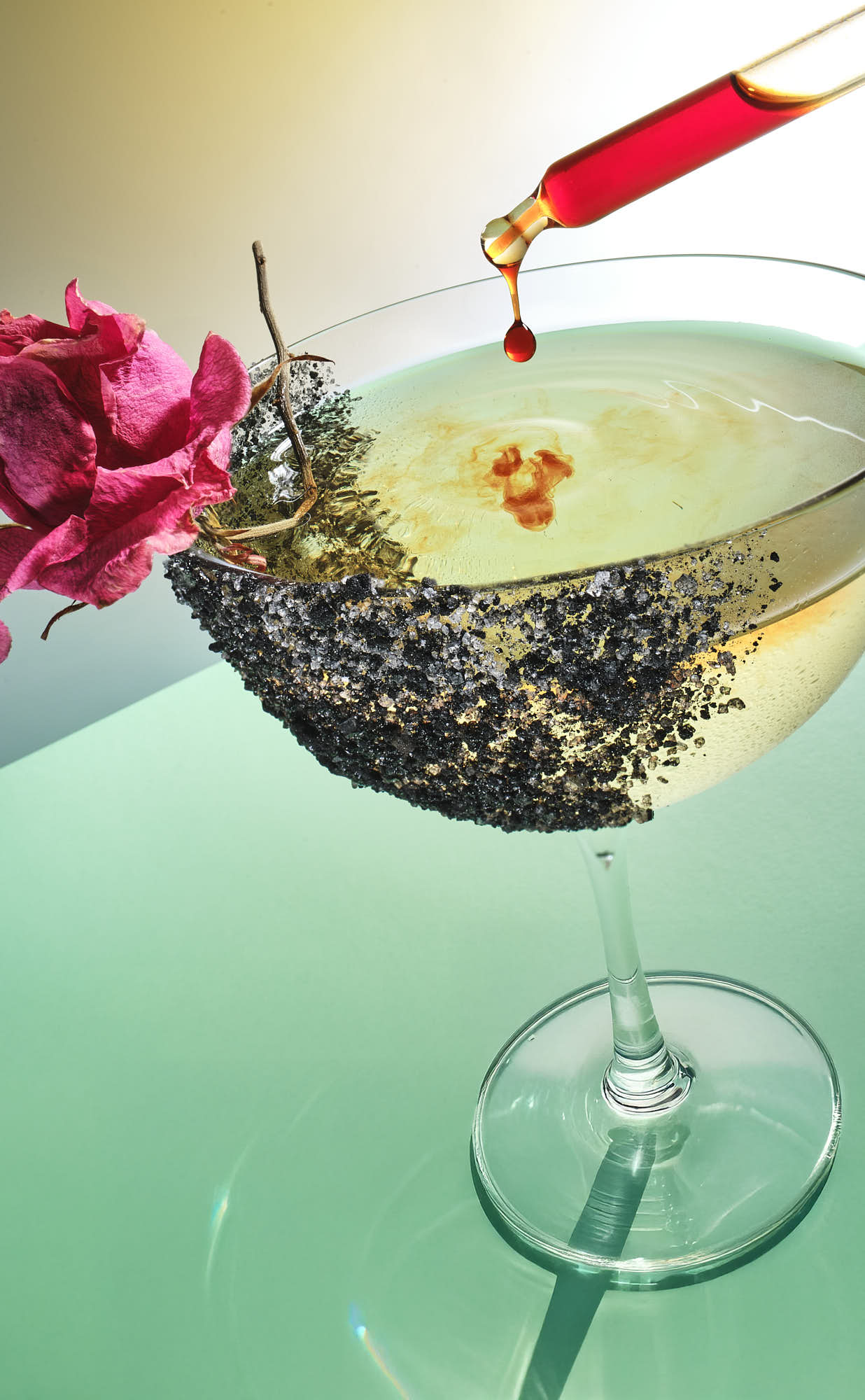 A colorful cocktail garnished with a flower, placed on a reflective surface with a subtle gradient background.