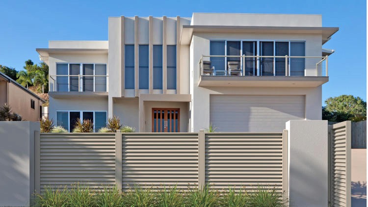 A modern home's outdoor patio area enclosed by a light grey louvered aluminum privacy fence.