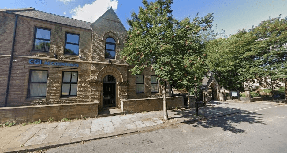 A gray-haired man in a dark suit smiles while shaking hands at a business event.