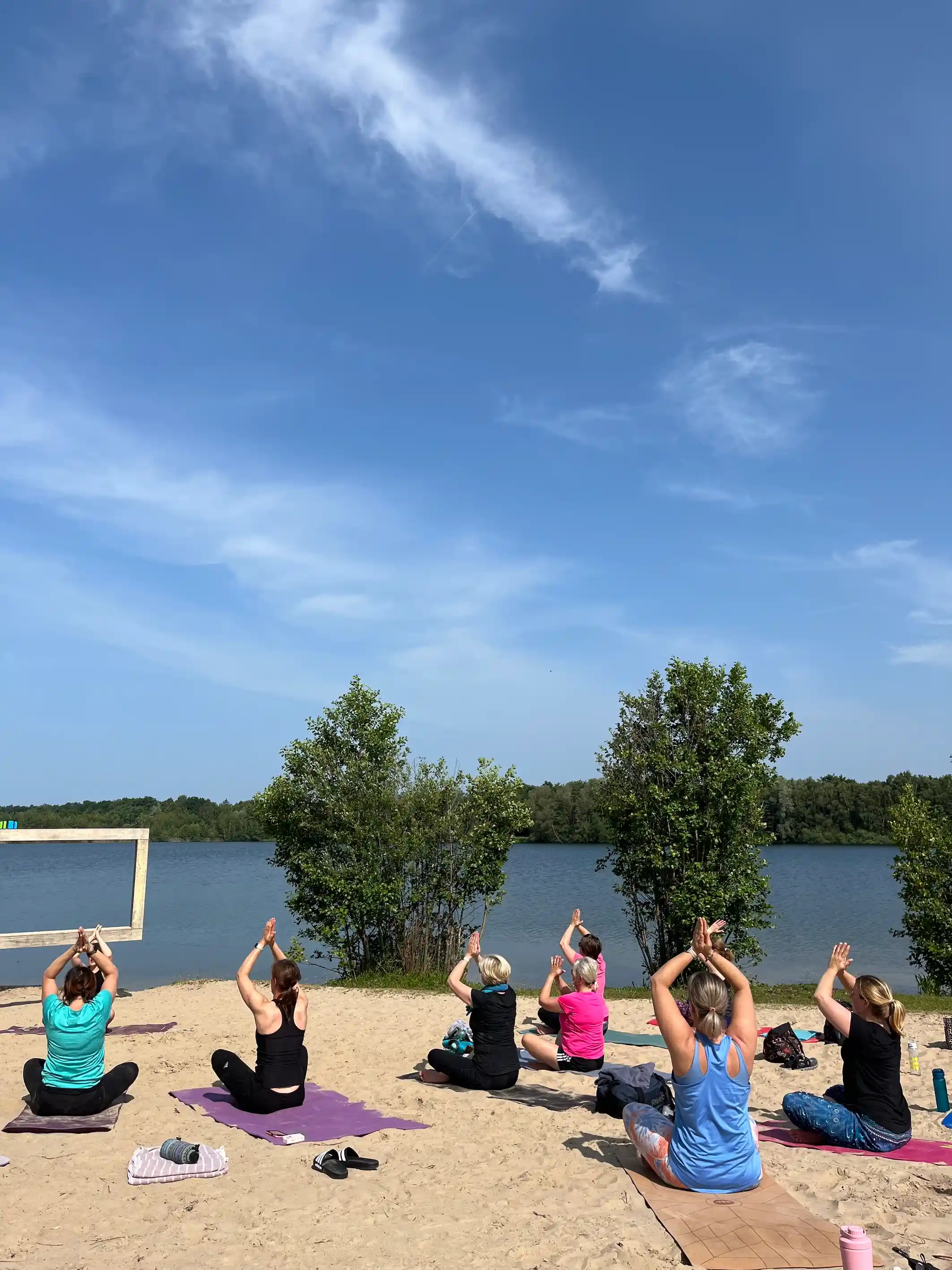 Menschen entspannen bei einer Yoga-Einheit am Dranländersee und genießen anschließend ein gesundes Picknick; Strong Partners fördert Employee Wellbeing und Betriebliches Gesundheitsmanagement durch aktive Firmen-Events.