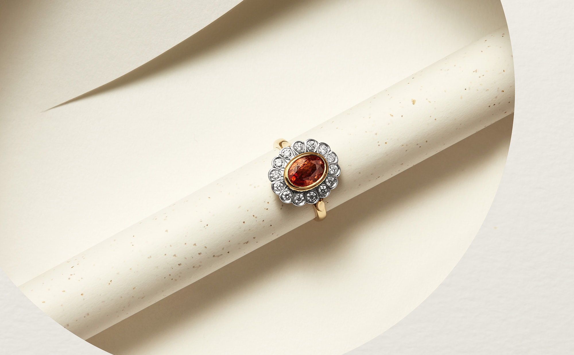 Elegant diamond and orange gemstone ring on a light textured background.