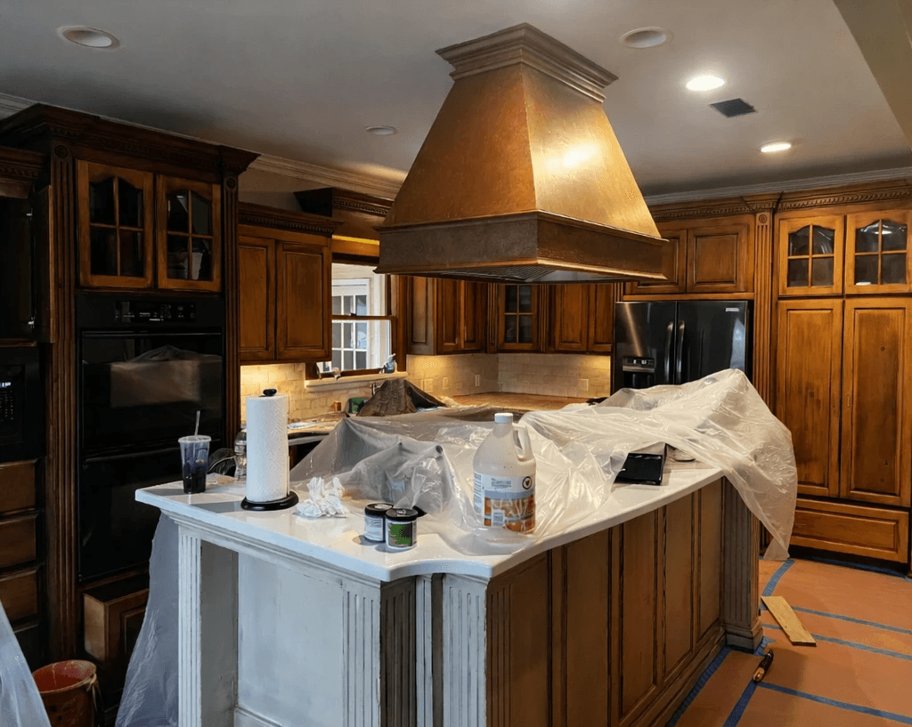 A modern, luxury beachfront villa with large glass windows and balconies overlooks a rocky shoreline, surrounded by palm trees at sunset.