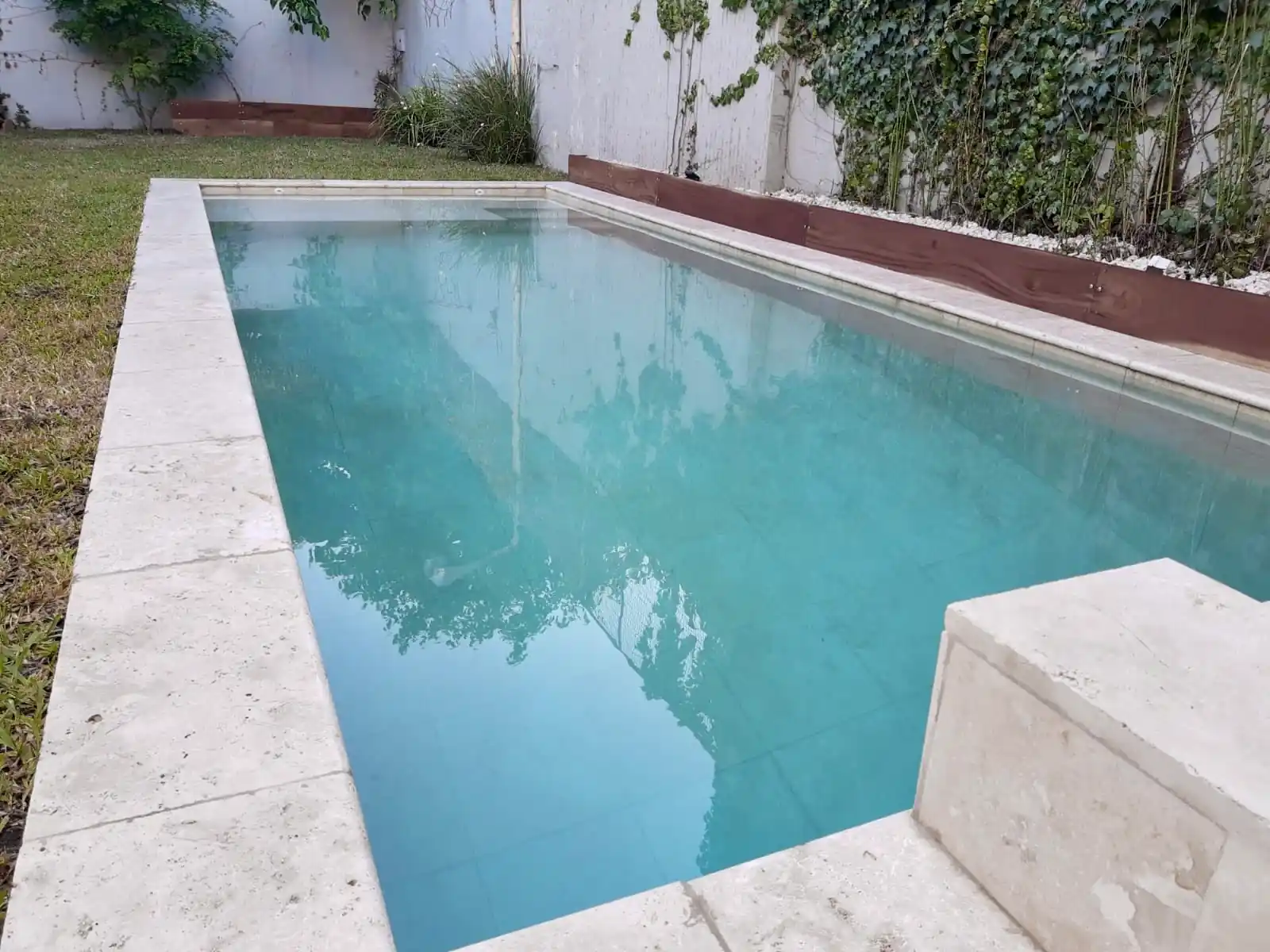 Moderna pileta optimizada para patios estrechos, con agua turquesa y terminaciones de lujo en mármol travertino claro.