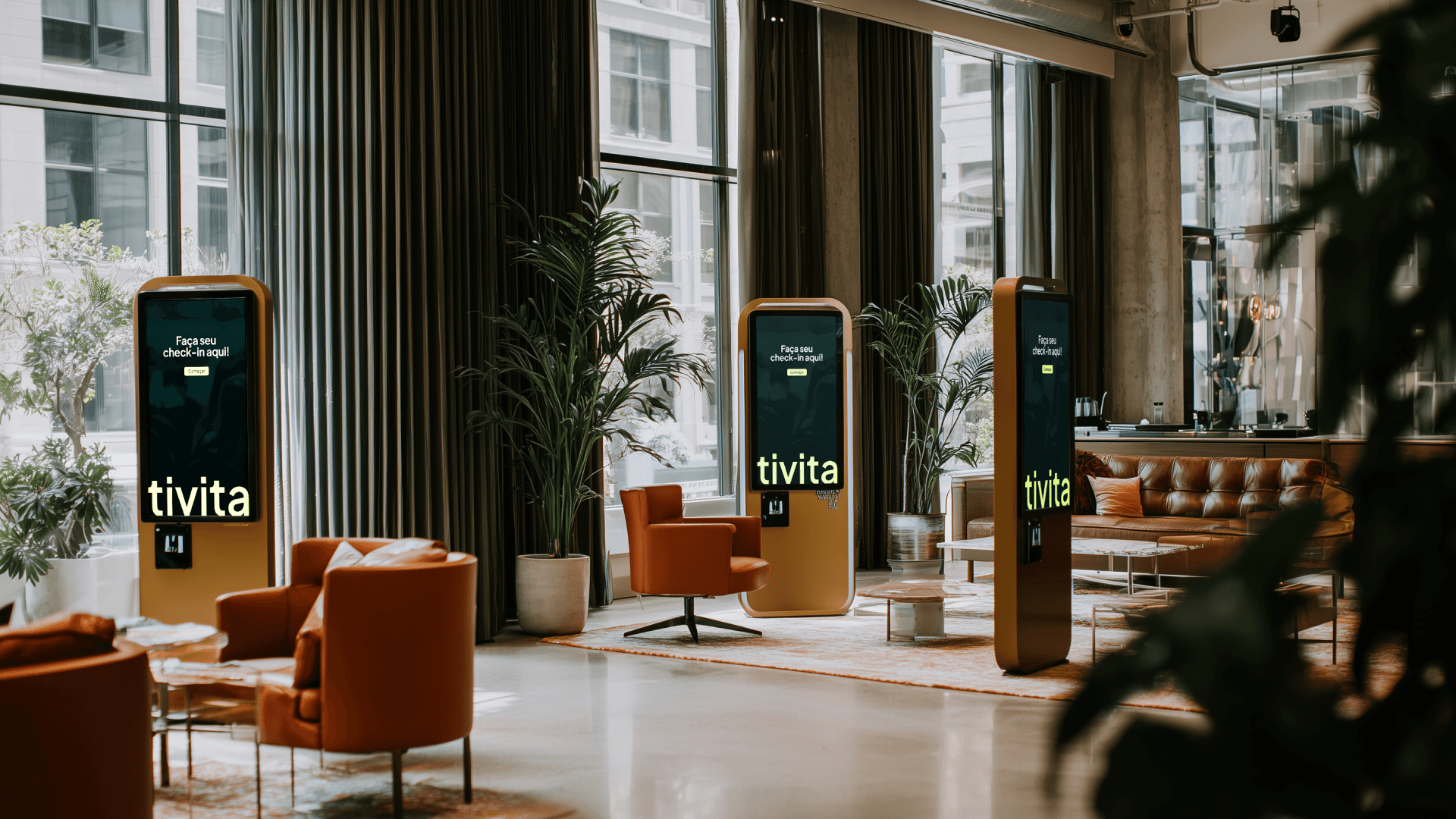 Recepção ampla e iluminada com sofás e cadeiras; três totens verticais da Tivita ao centro com tela de check-in, cenário de entrada e organização para clínicas.