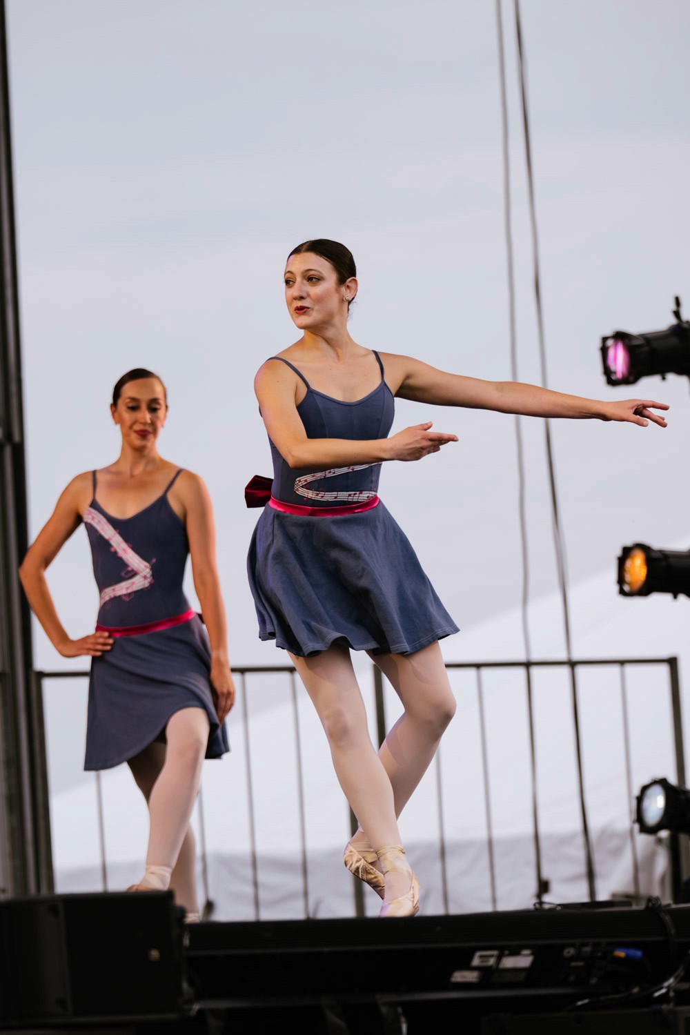 Two ballet dancers perform outdoors in daylight.