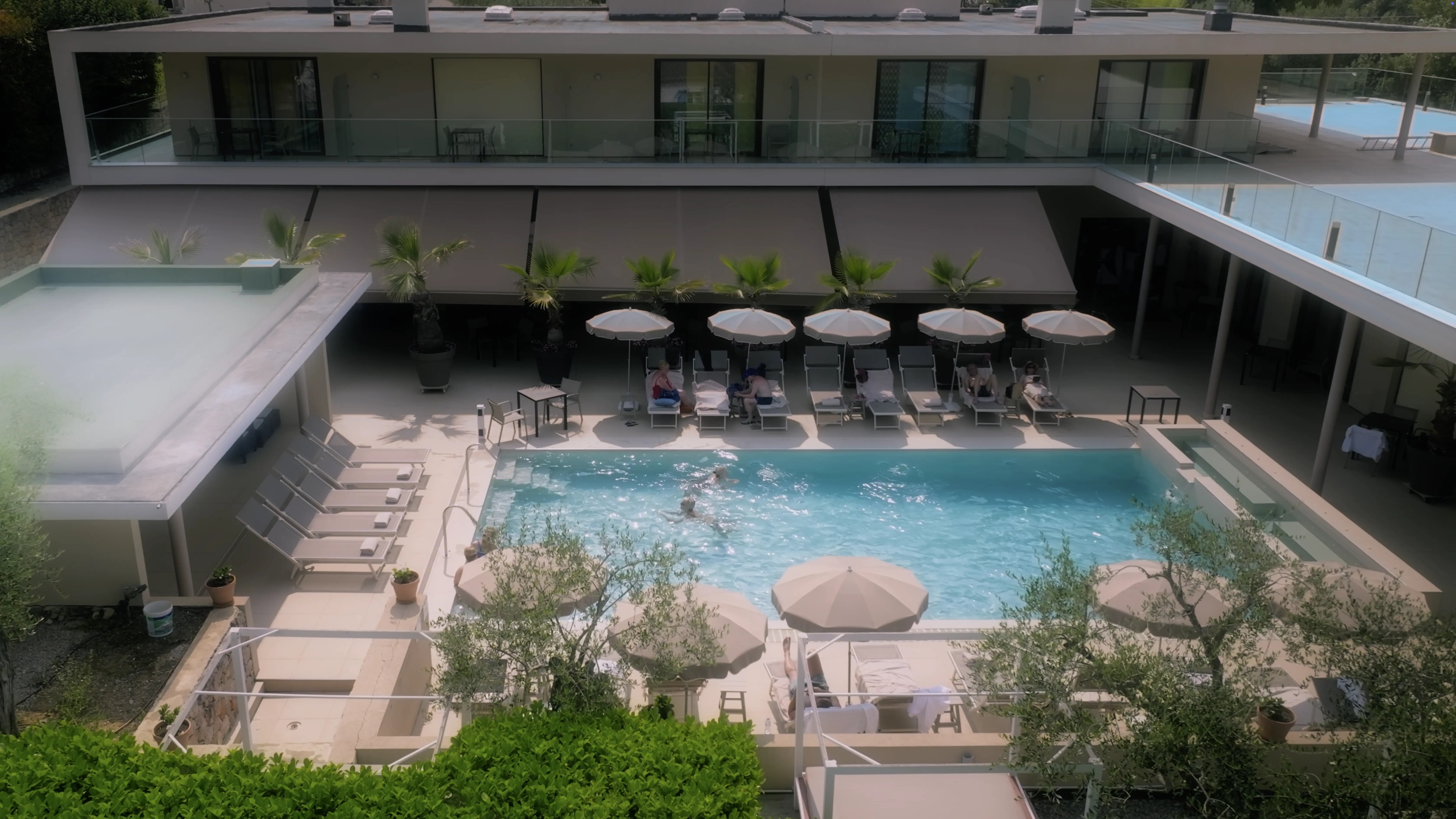 A luxurious, modern villa features a spacious outdoor area with a pristine swimming pool, surrounded by lounge chairs and umbrellas, creating an inviting space for relaxation and leisure.