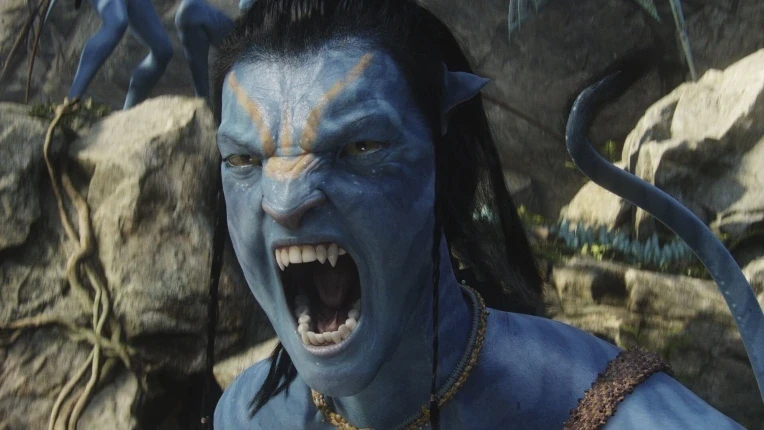 A blue-skinned, humanoid Na'vi character with sharp teeth and pointed ears is mid-roar against a natural, rocky background. The figure has dark hair and wears beaded jewelry, conveying a sense of intensity and emotion.