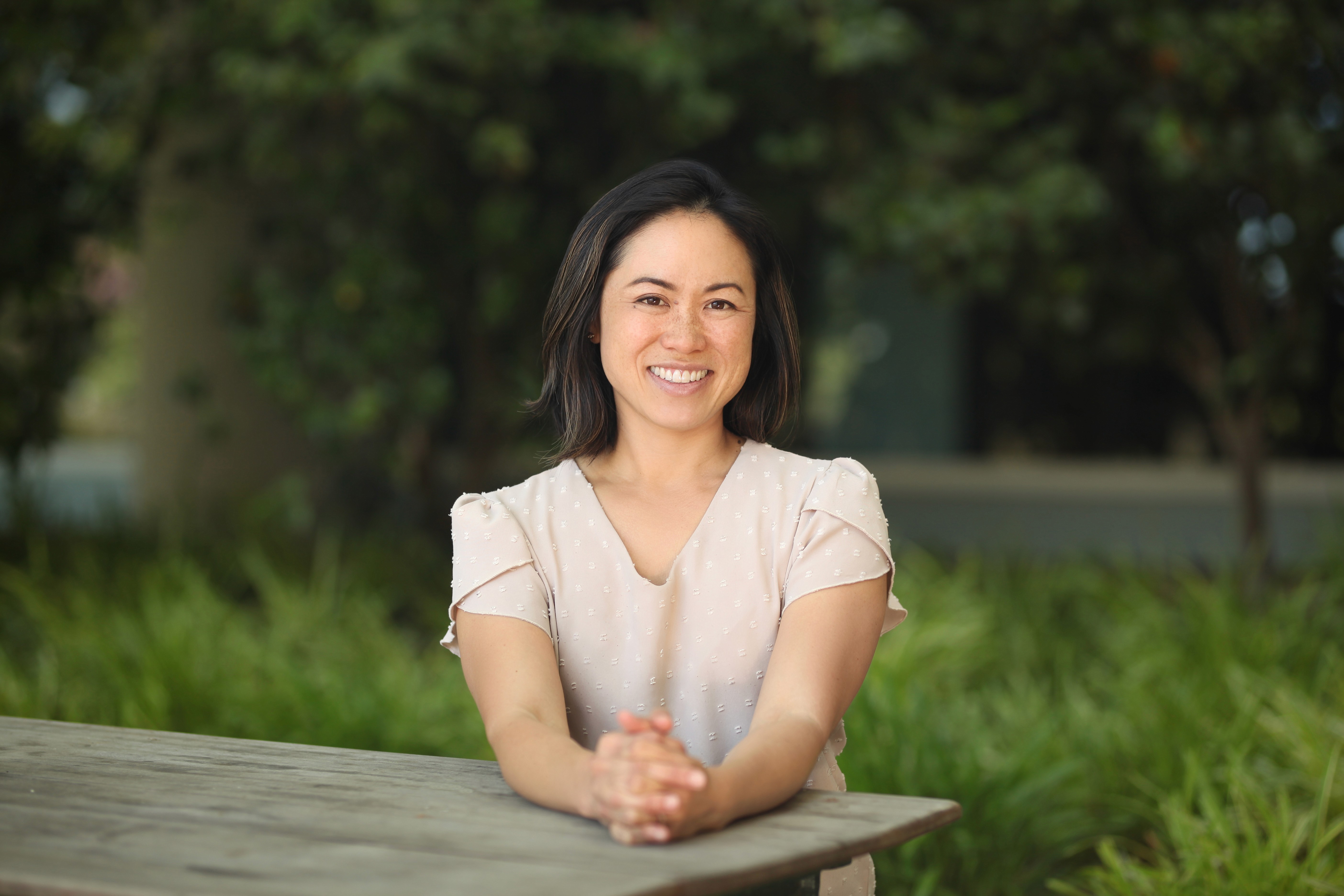 Julie Ownes sitting at wooden table in dress shirt, nature background