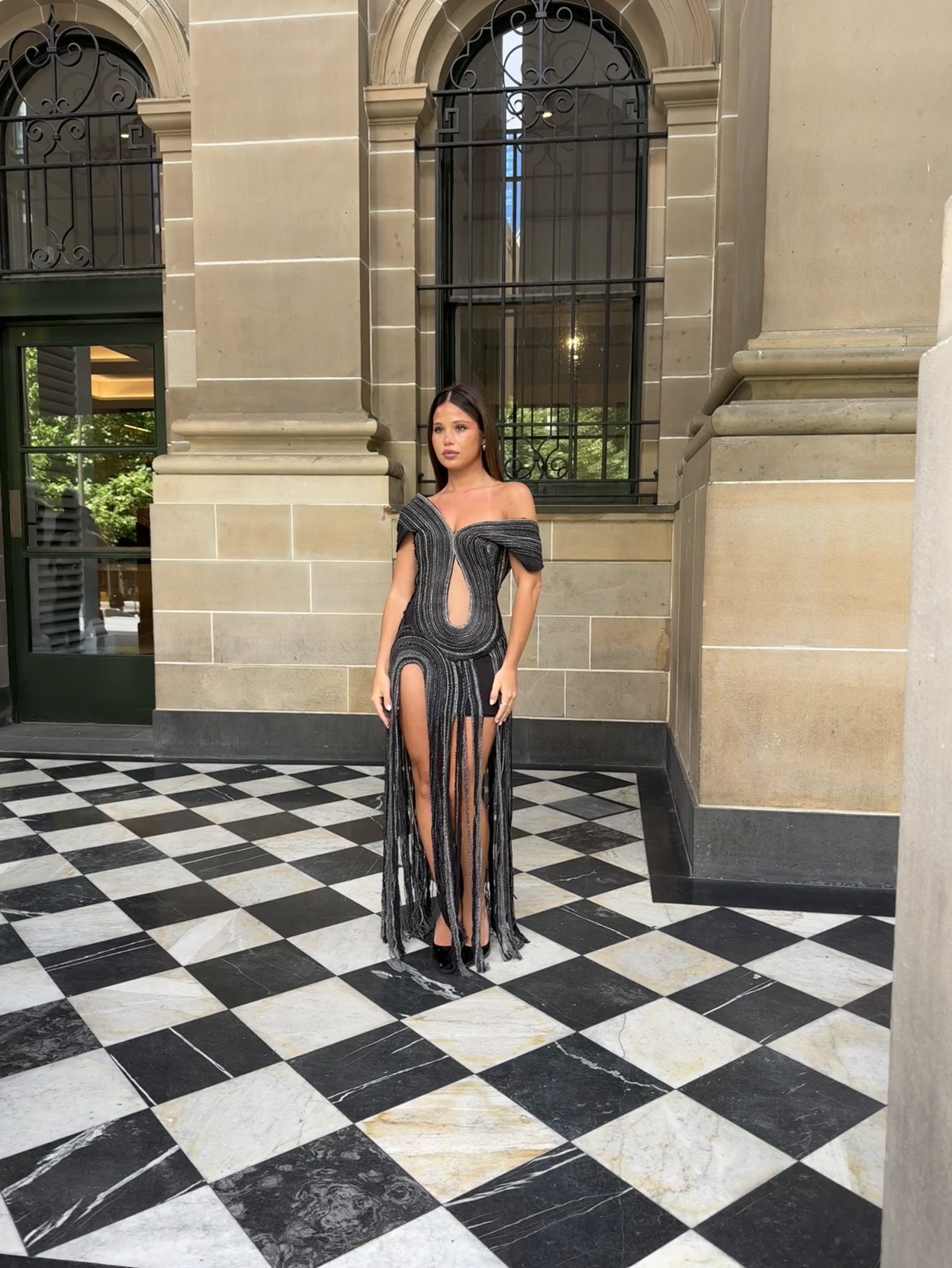 Floor-length black beaded gown with off-shoulder neckline, sculpted bodice cut-out, and elongated fringe skirt with front slit