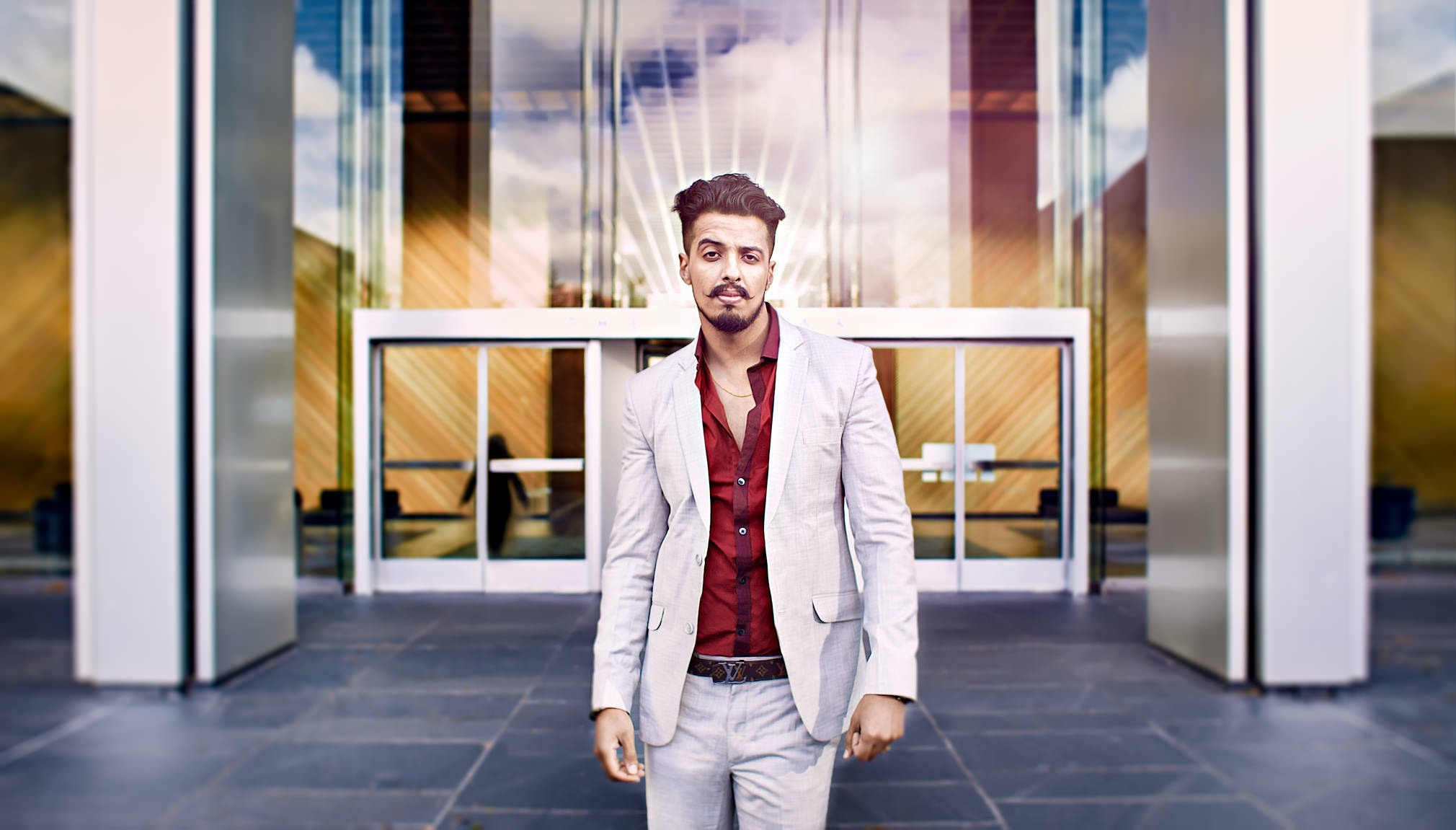 Outdoor environmental headshot of South Asian man in light suit standing in front of modern office building in Oakland California