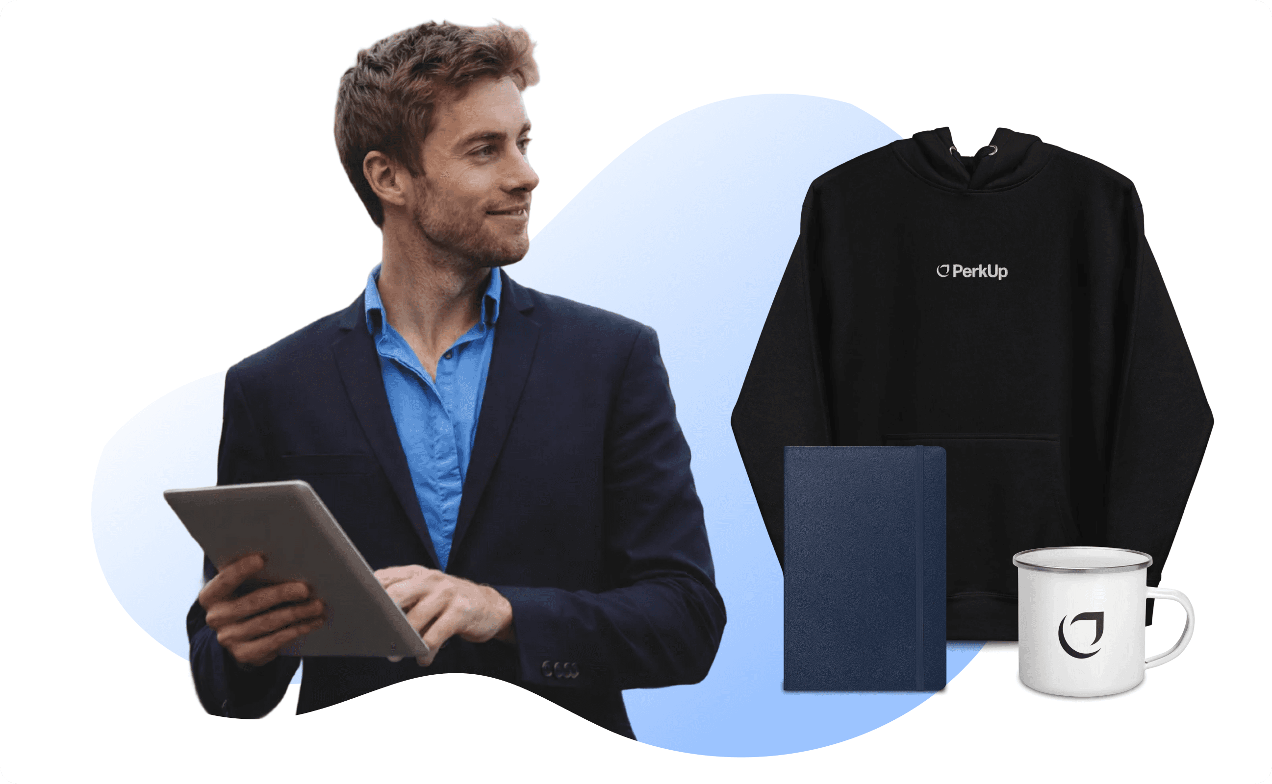 A man holding a tablet. Beside him are a notbeook, a mug, and a hoodie.