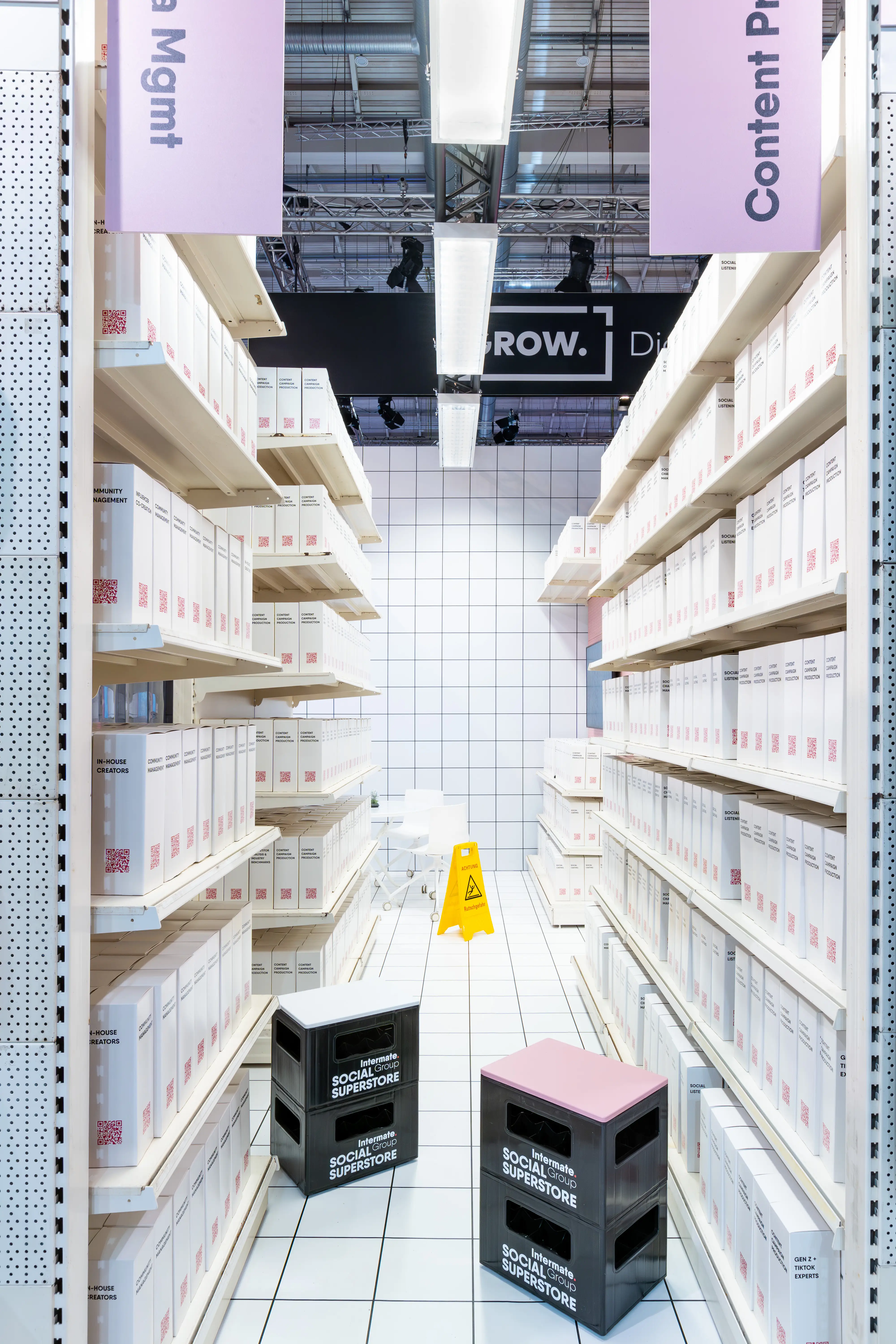 Supermarket aisle of the Intermate Social Superstore at OMR with white product boxes on shelves and black beverage crates.