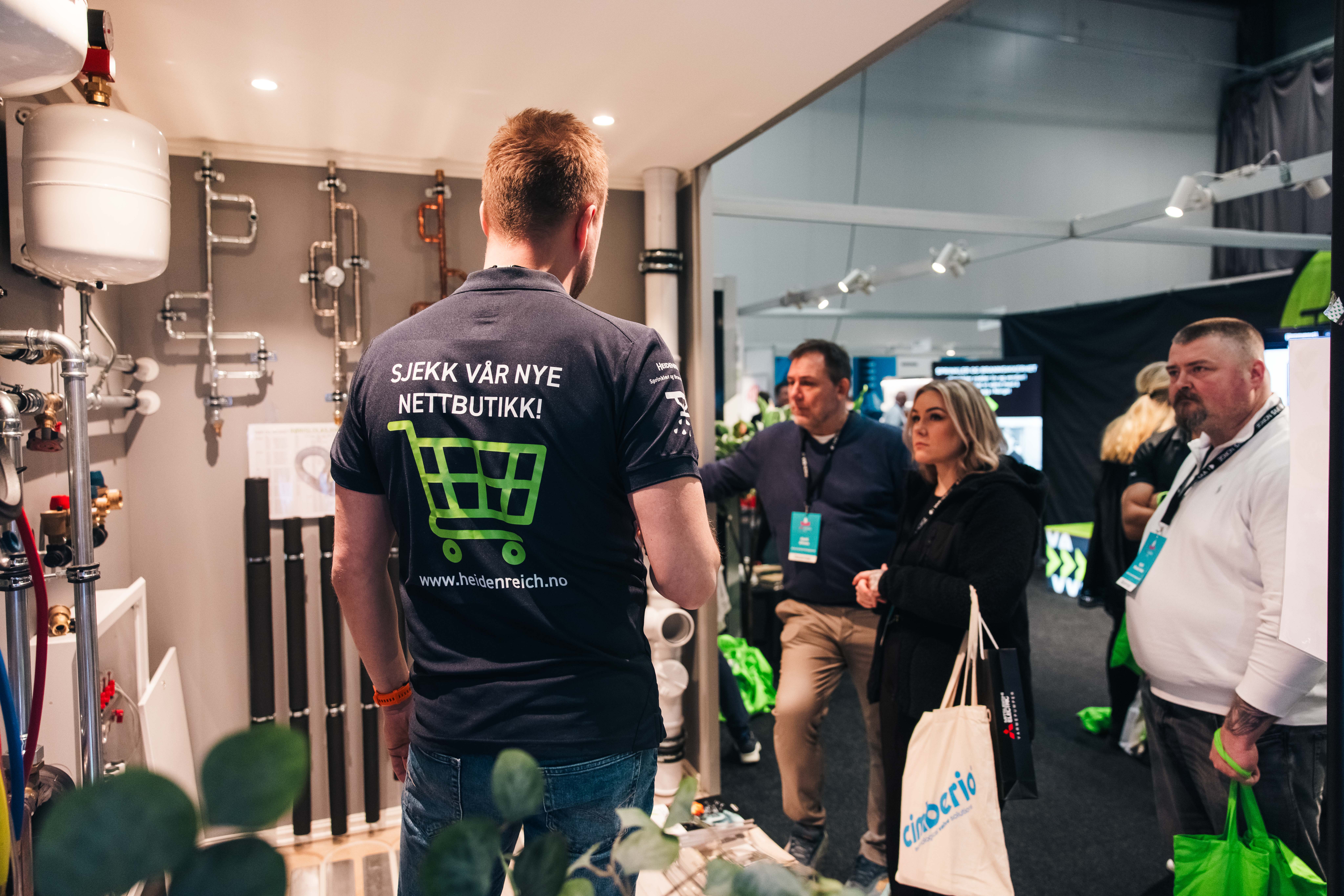 Folk som interessert ser på messestand mens leverandør med ryggen til forteller om nye produkter og løsninger