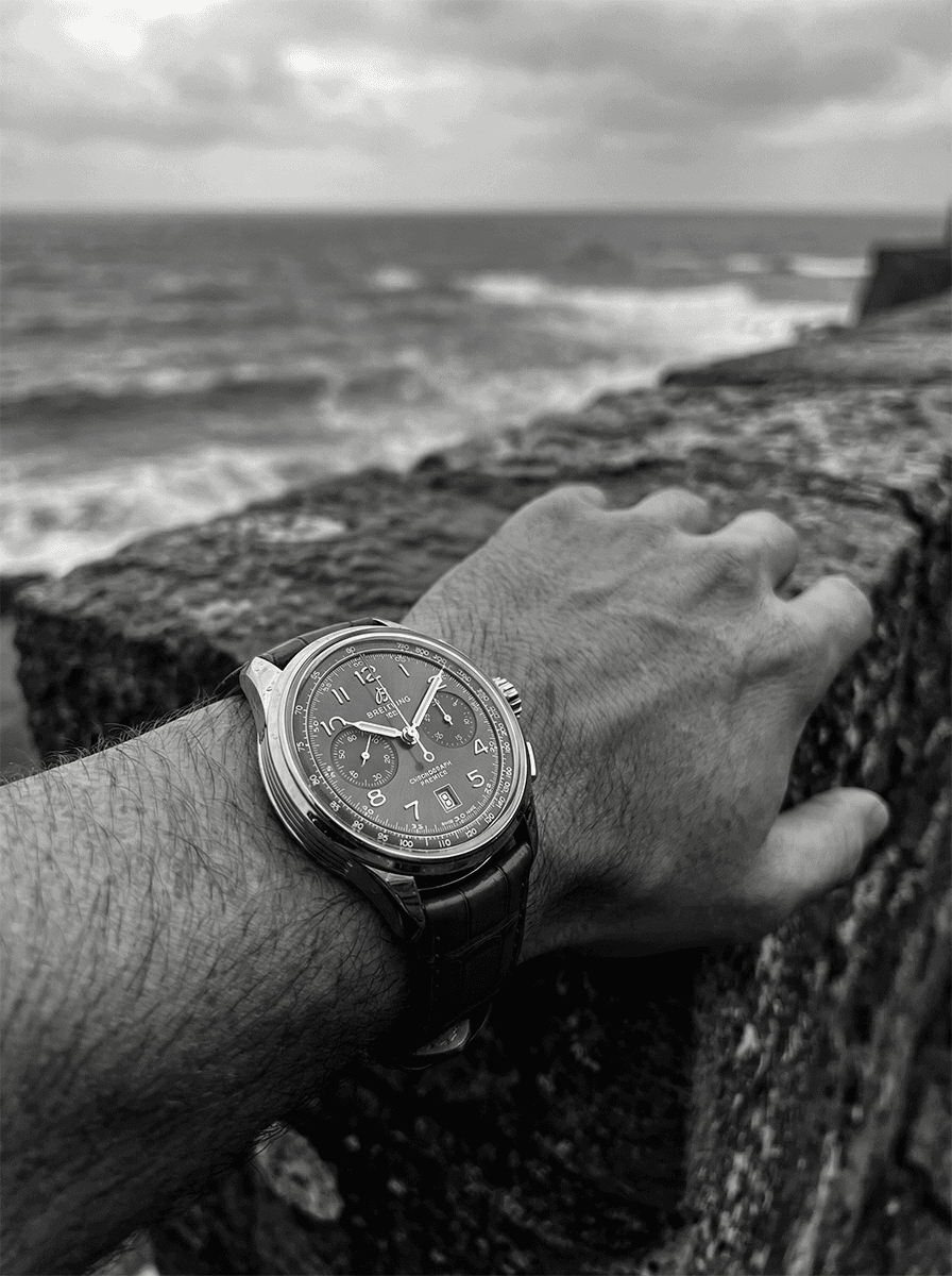 Close-up black and white photography of a wristwatch overlooking the sea, symbolizing time and reflection.