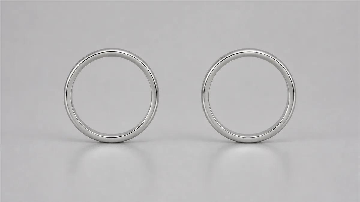 Two nearly identical plain silver rings stand upright on a pale-grey surface
