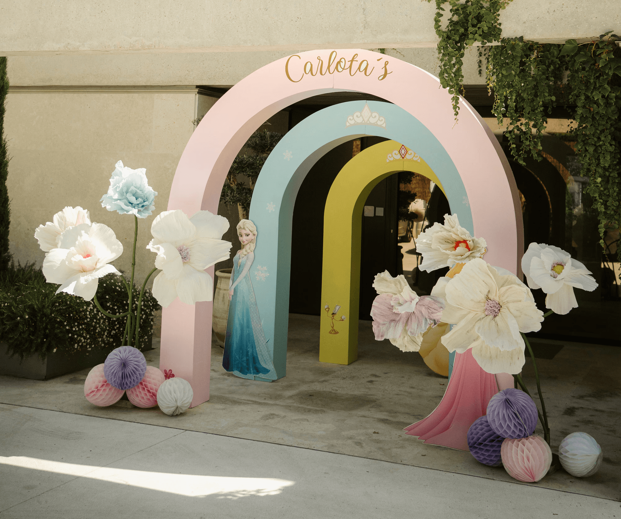 Pastel princess party entrance with rainbow arches, flowers, and character décor