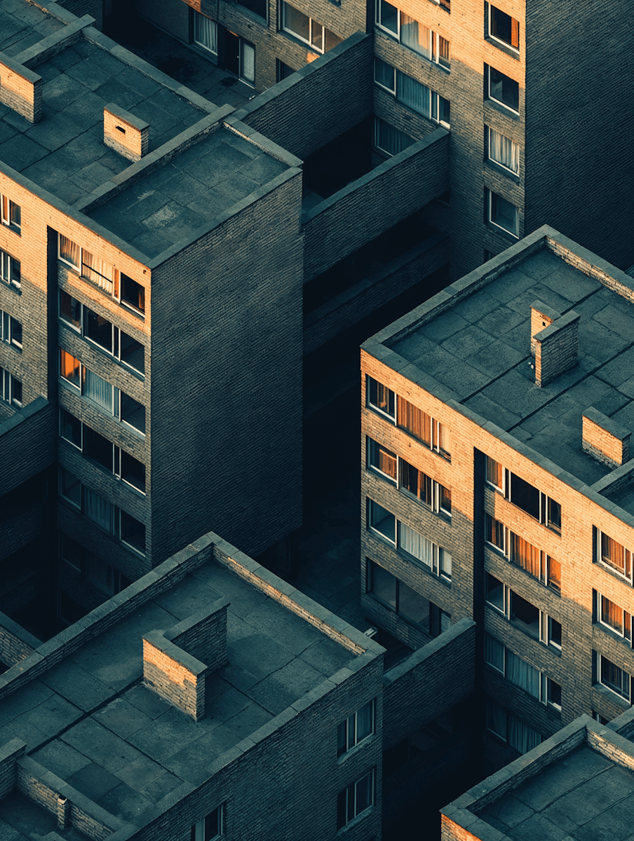 Aerial view of modern apartment buildings with geometric rooftops, brick facades, and warm window light.