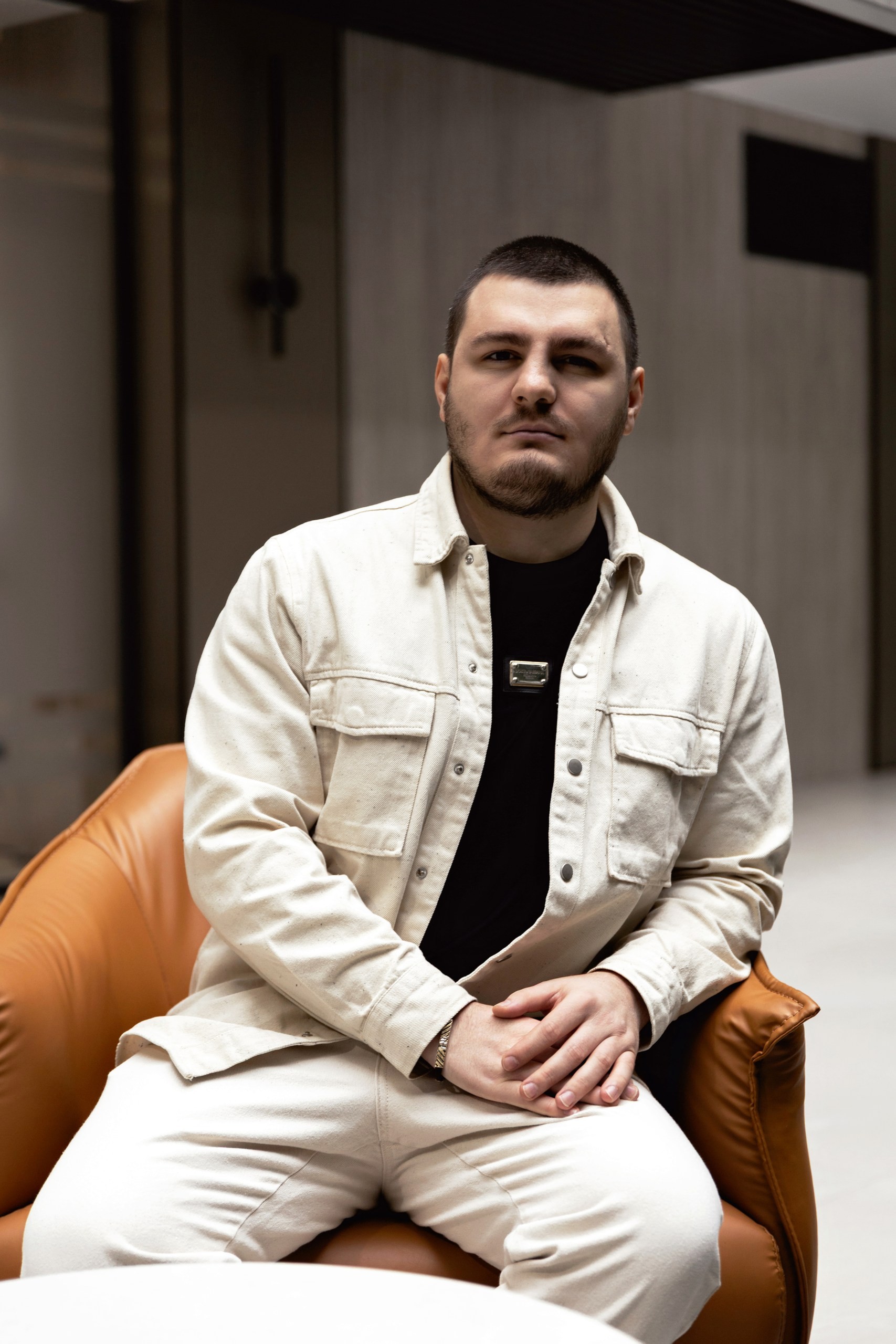 Casual studio portrait of a bearded man with curly hair in a white shirt, arms crossed, on a light gray background.