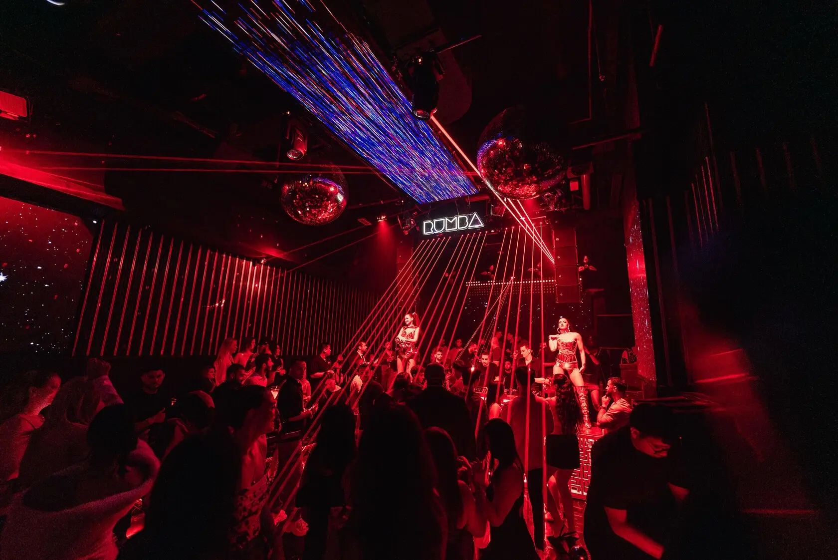 Red laser show over the dance floor at The Myth Dubai, with dancers on podiums under the Rumba sign