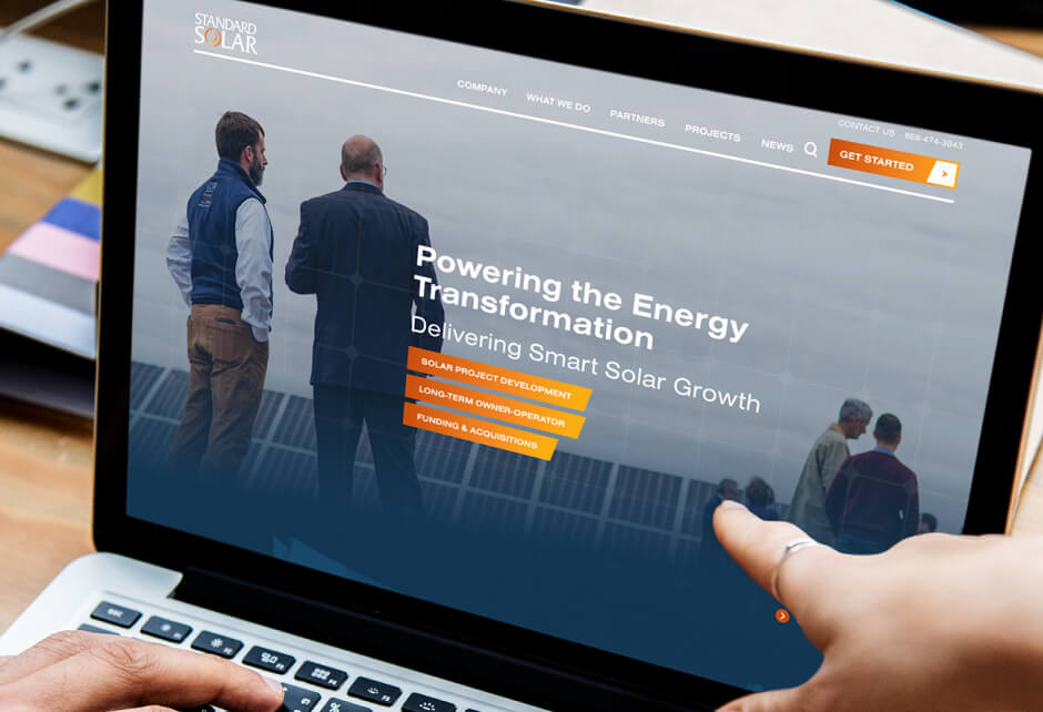 A person points at a laptop screen displaying the Standard Solar website, where two men discuss energy transformation and solar project development, highlighting brand authenticity and a core truth in connecting with customers.