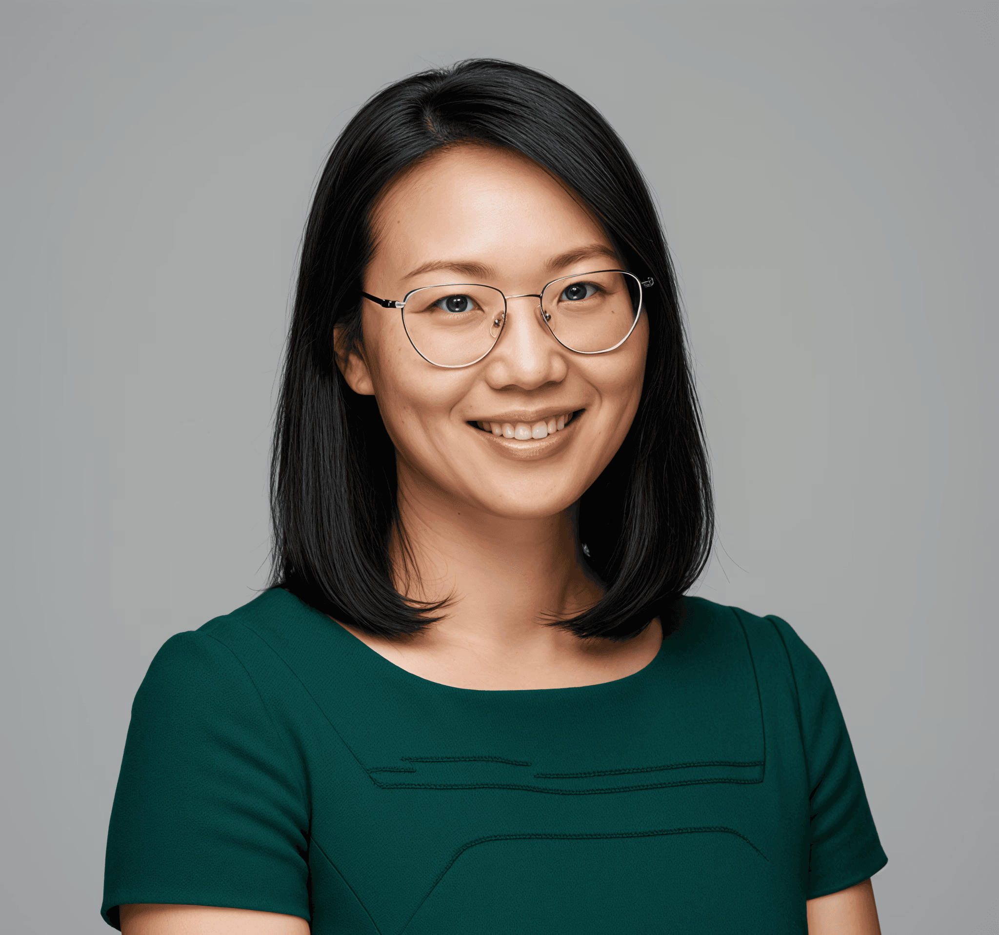 Portrait of a woman with glasses and shoulder-length black hair, green top, smiling.