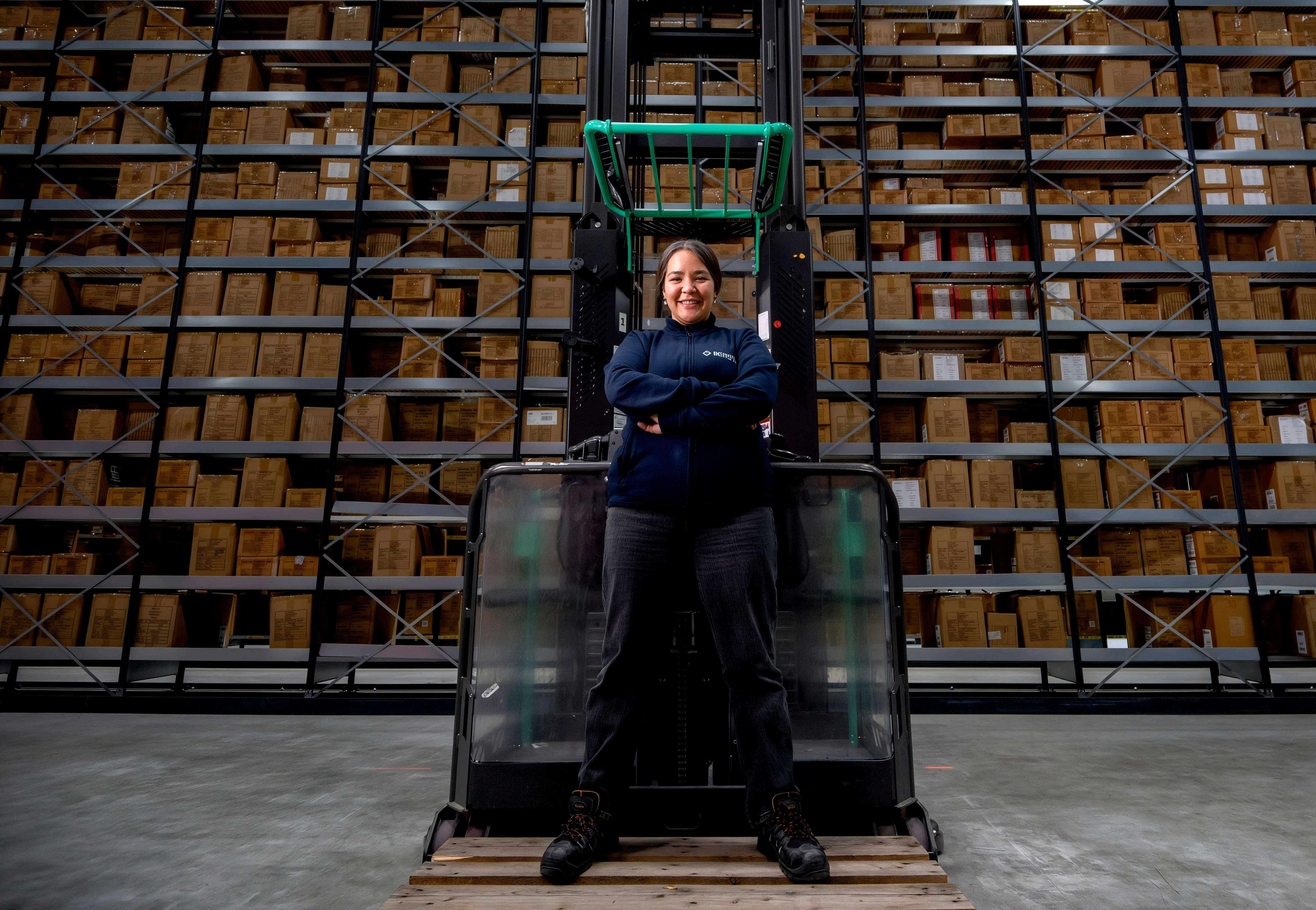 Kvinna står stolt framför en truck med armarna i kors i ett lager fyllt med lådor.