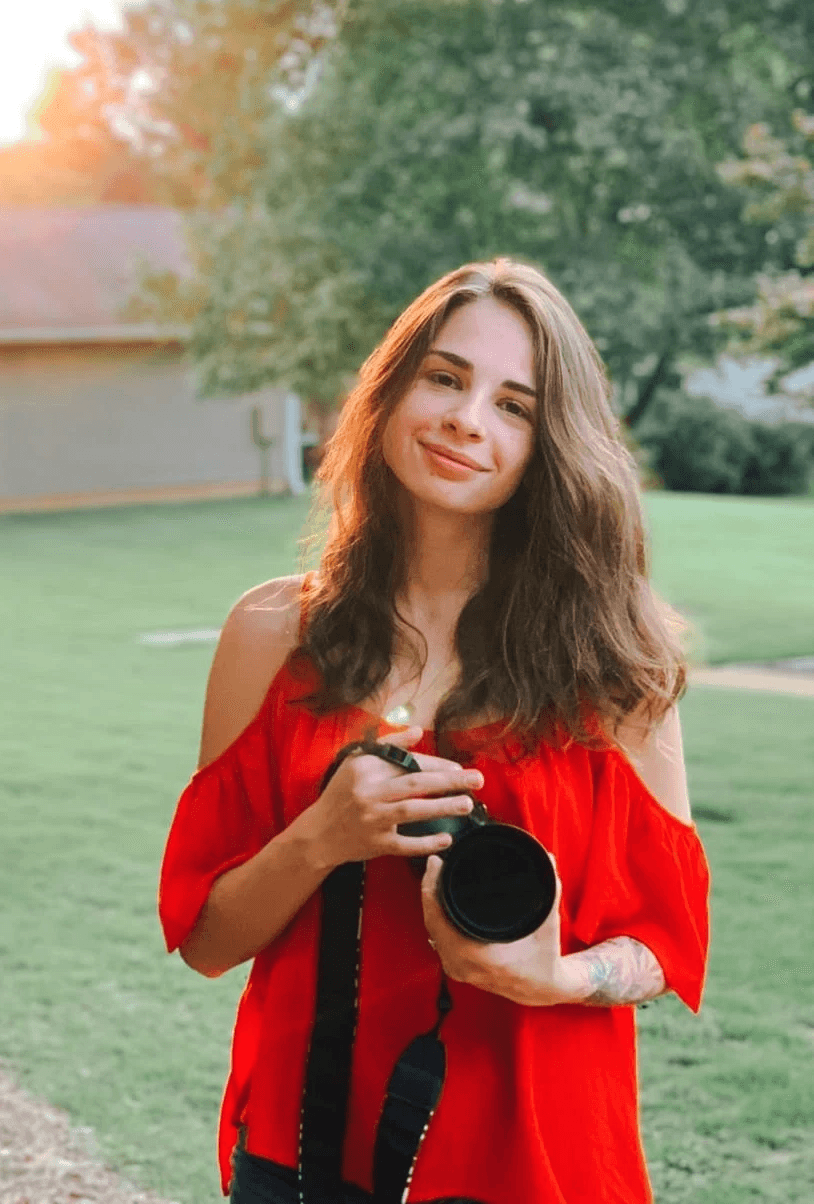 A person with short blonde hair holds a vintage camera.