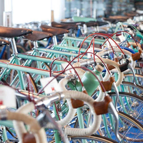 ردیف‌هایی از دوچرخه‌های قدیمی با زین‌های چرمی و دسته‌های رنگارنگ در نمایشگاه چیده شده‌اند.