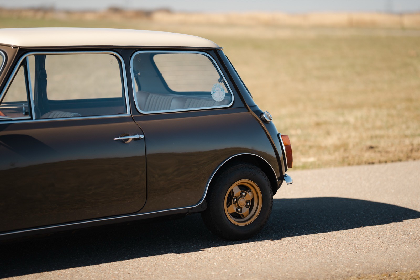 A vintage car with a two-tone paint job parked on a road, set against a grassy landscape.