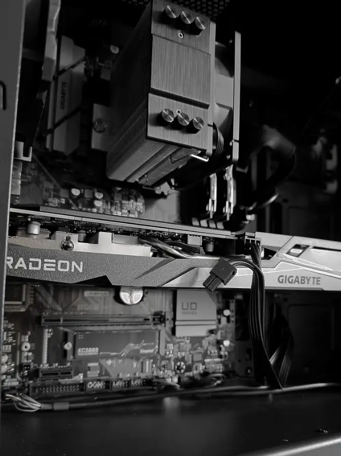Czarno-białe zdjęcie wnętrza komputera z bliska. W centralnej części widoczna jest karta graficzna Gigabyte Radeon, a poniżej dysk Kingston KC3000 zamontowany na płycie głównej Gigabyte z serii UD. U góry znajduje się masywne, wieżowe chłodzenie procesora.