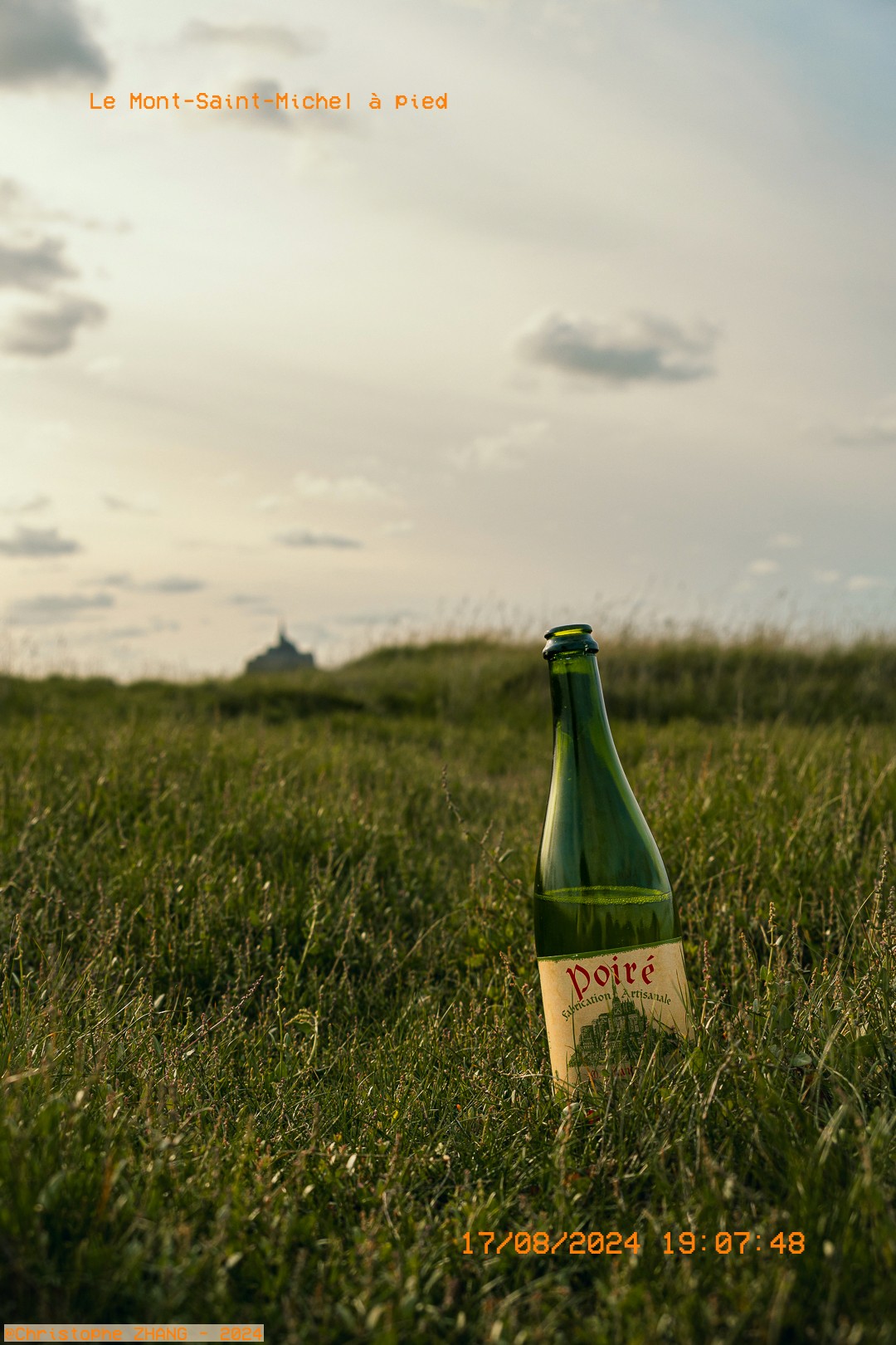 Bouteille de poiré au sol avec le Mont Saint-Michel au loin.