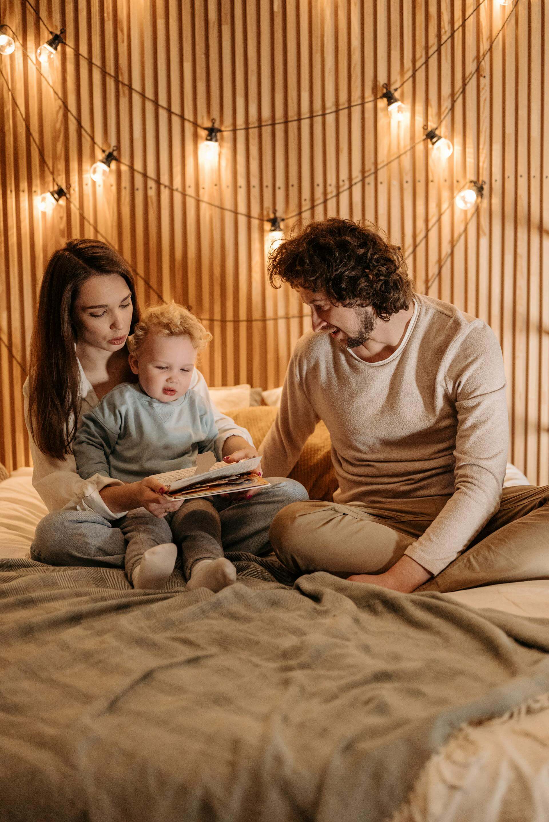 A man and woman sitting on a bed, lovingly gazing at their baby nestled between them