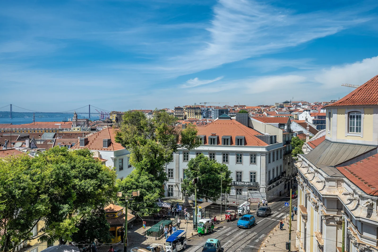 Lisbon rooftops and city streets with the 25 de Abril Bridge in the distance.