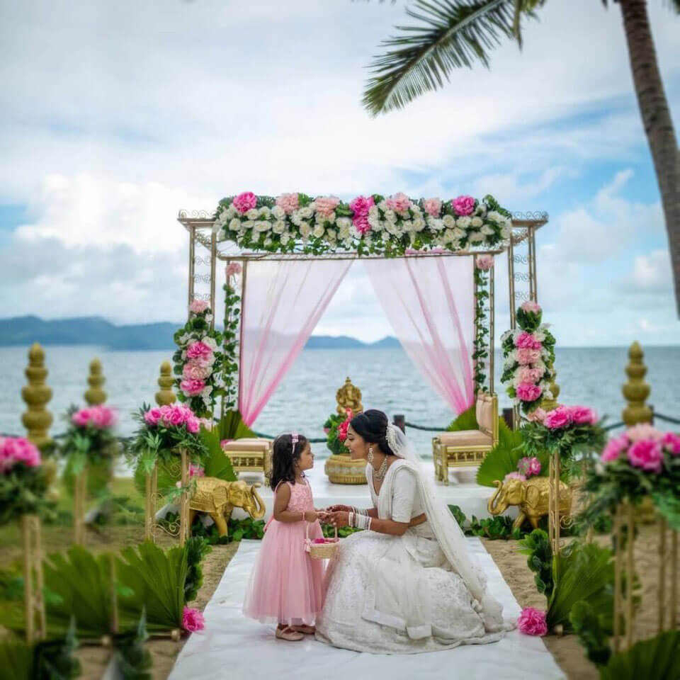 Bride and flower girl on a white aisle at a tropical beachfront Indian style wedding ceremony setup, Uprising Beach Resort.