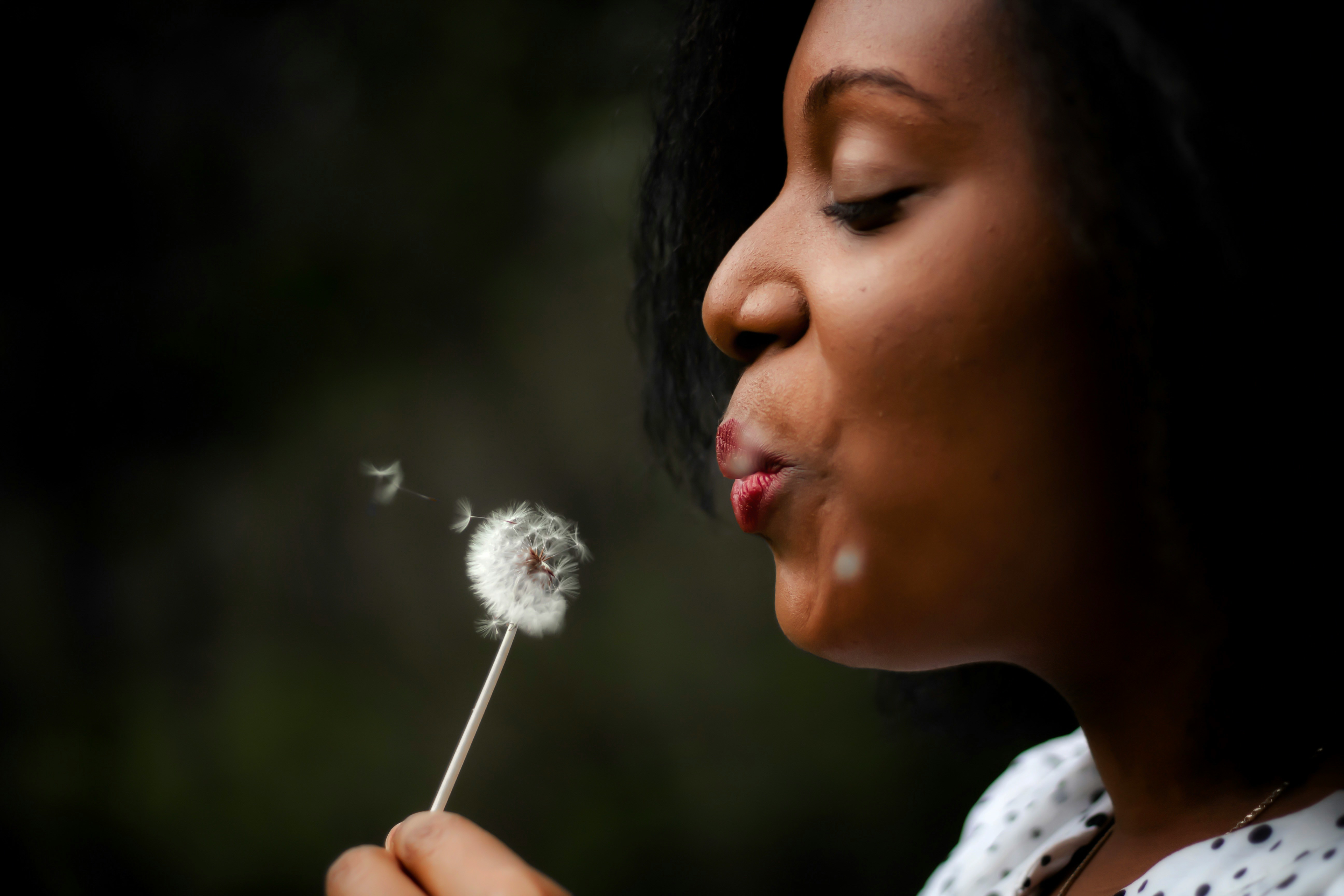 Woman in white top blowing a dandelion