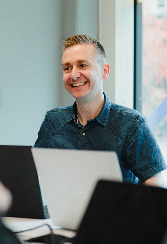 A young man in a white t-shirt stands against a light-colored background.