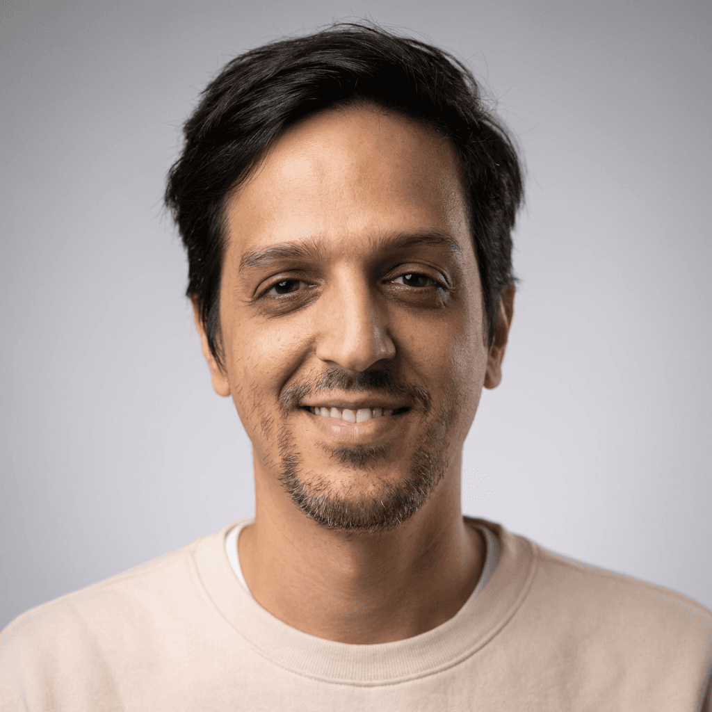 Portrait of a smiling man in a plaid button-up shirt against a gray background.