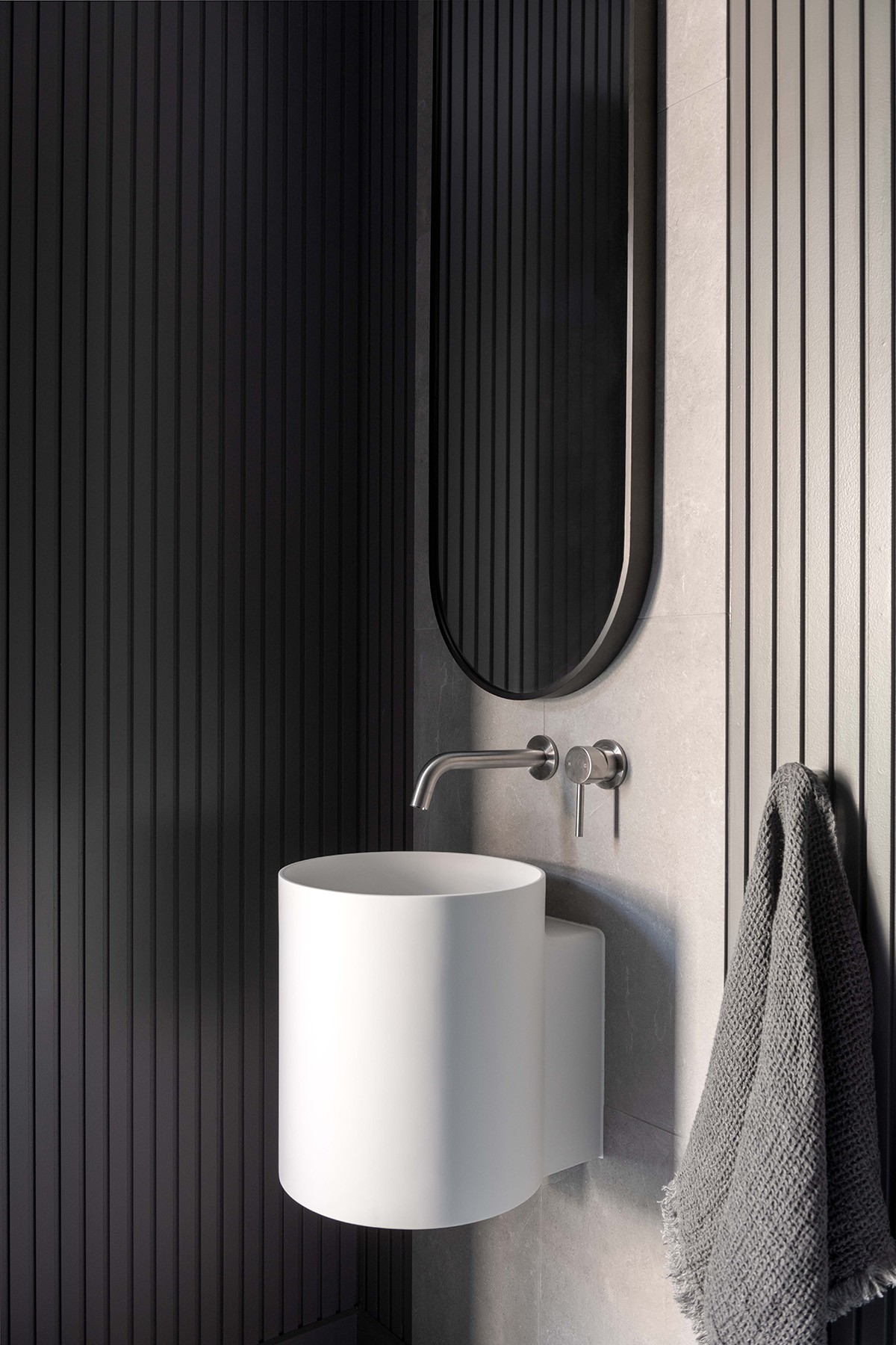 Bathroom detail at The Stables featuring a sculptural basin, vertically lined walls, and minimal fixtures within a dark, tactile interior.