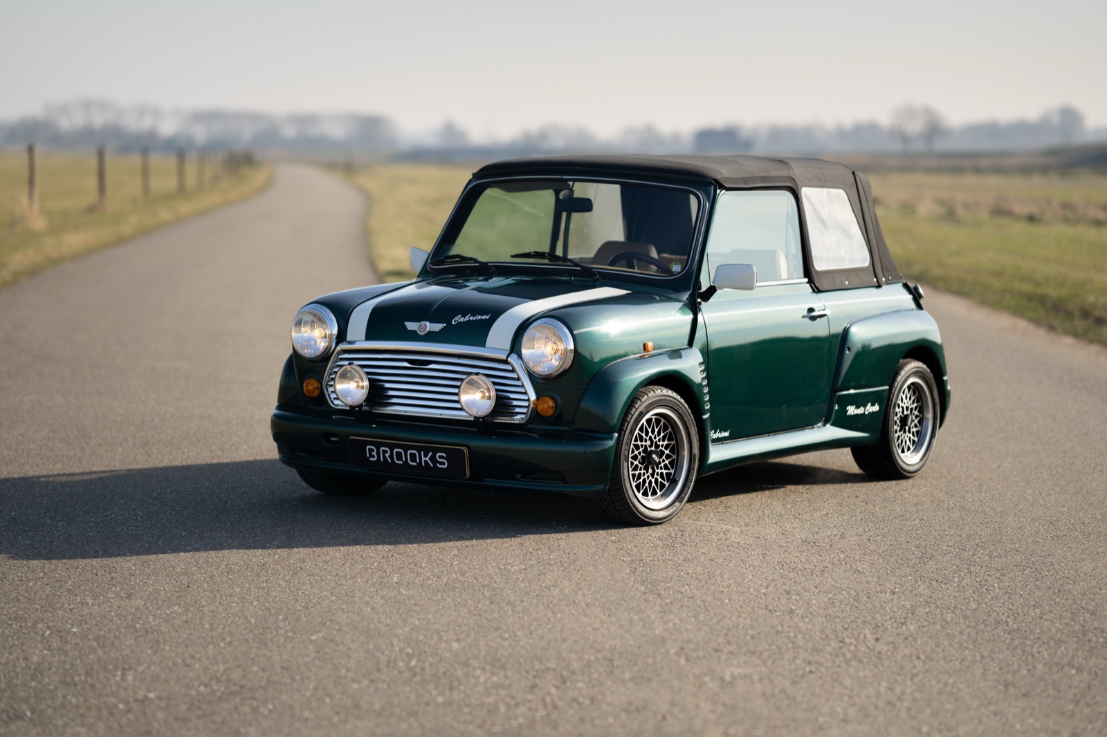 A green and black compact car parked on an empty road, surrounded by open fields under a clear sky.