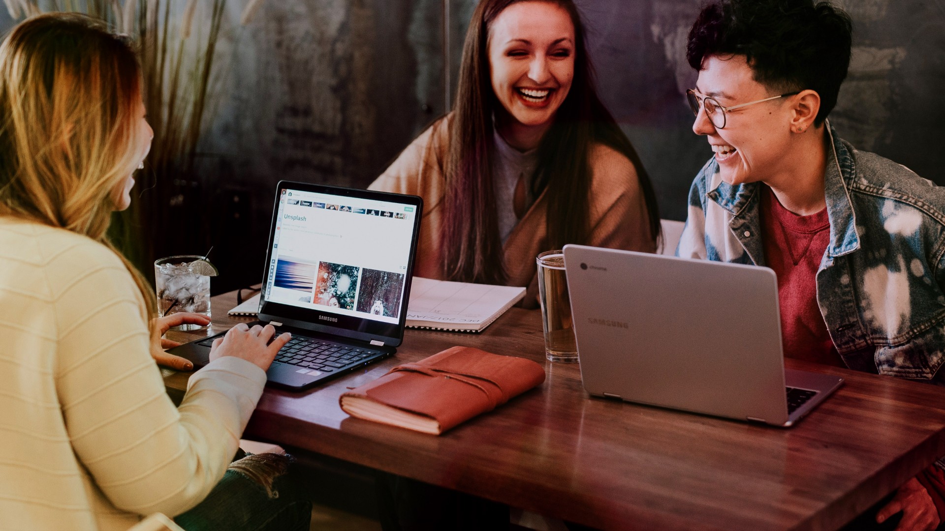 Women laughing together while working at a table with laptops
