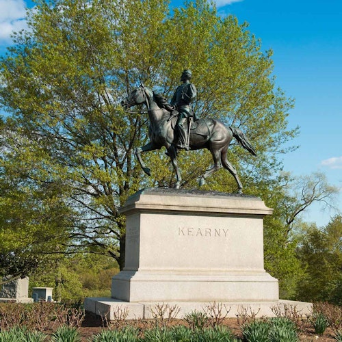 تمثال فروسية لفارس يُدعى كيرني، موضوع على قاعدة حجرية في حديقة ذات أشجار خضراء وسماء زرقاء.