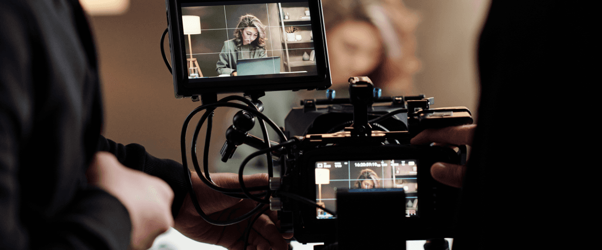 A professional video camera on a set filming a woman working on a laptop, representing how slow motion and time lapse videos can transform a brand film.
