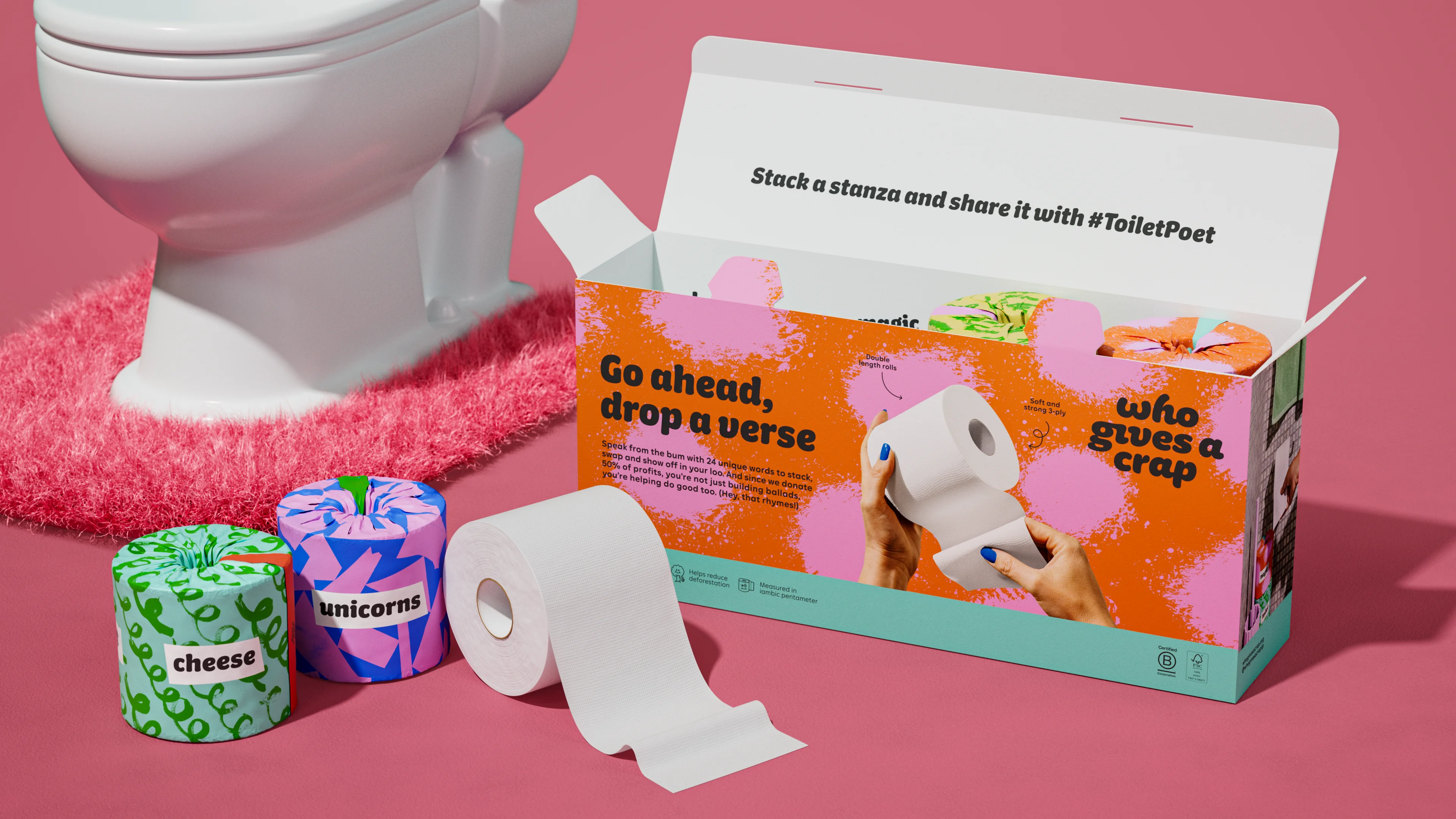 Open Who Gives A Crap Poetry Toilet Paper box beside a toilet, rolls labeled cheese and unicorns and an unrolled white roll on a pink floor